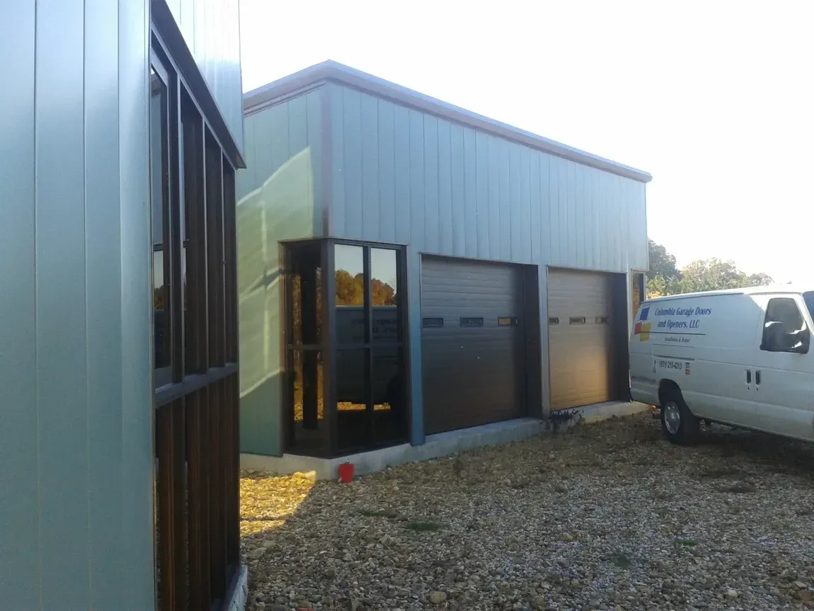 Metal workshop with garage doors and a white van parked outside on a gravel lot.