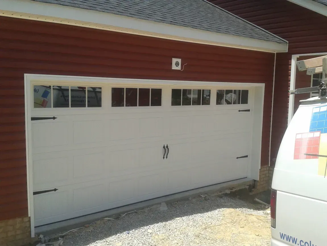 White garage door on a red brick house with small windows above it.