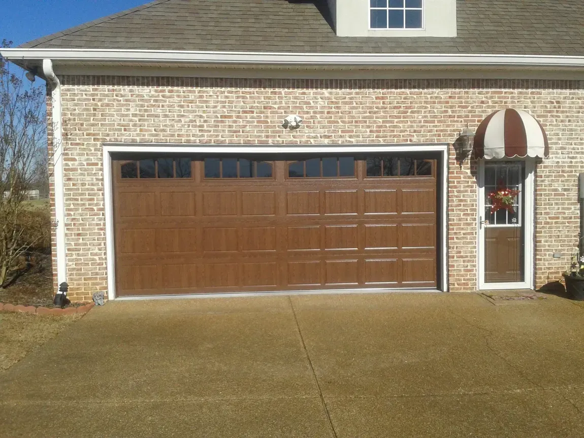 Brick house with a brown garage door and a small striped awning over the front door. Brick house with a brown garage door and a small striped awning over the front door.