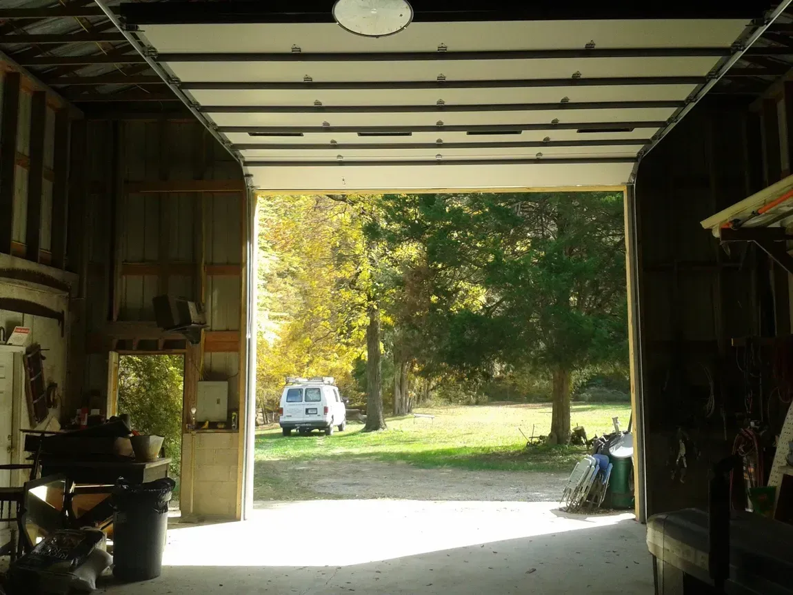 View from inside a garage to a sunny yard with a white van and trees outside