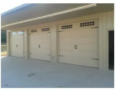 Three beige garage doors on a concrete driveway under a covered carport