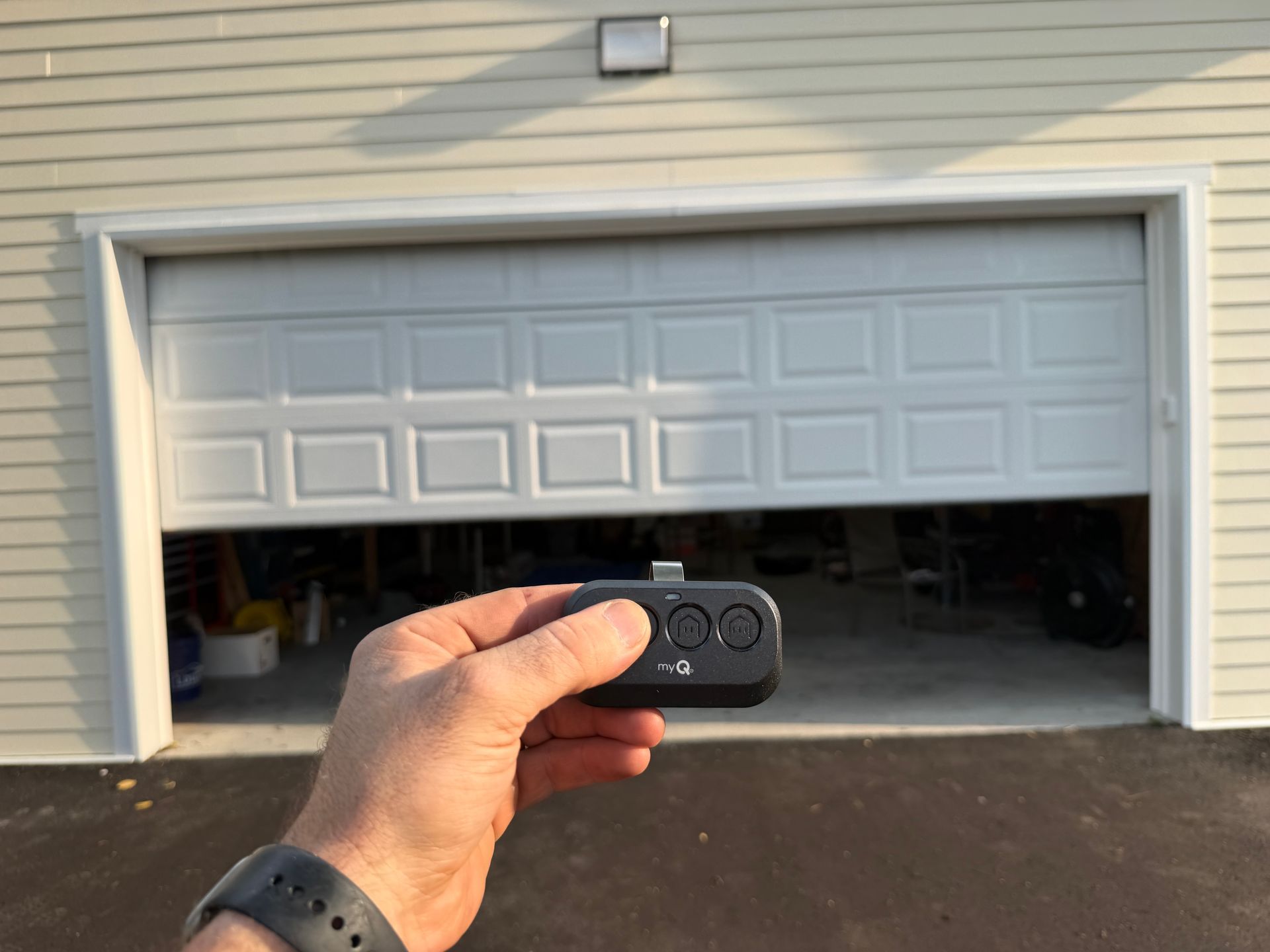 Hand holding a remote aimed at a partially open garage door with a car inside Hand holding a remote aimed at a partially open garage door with a car inside