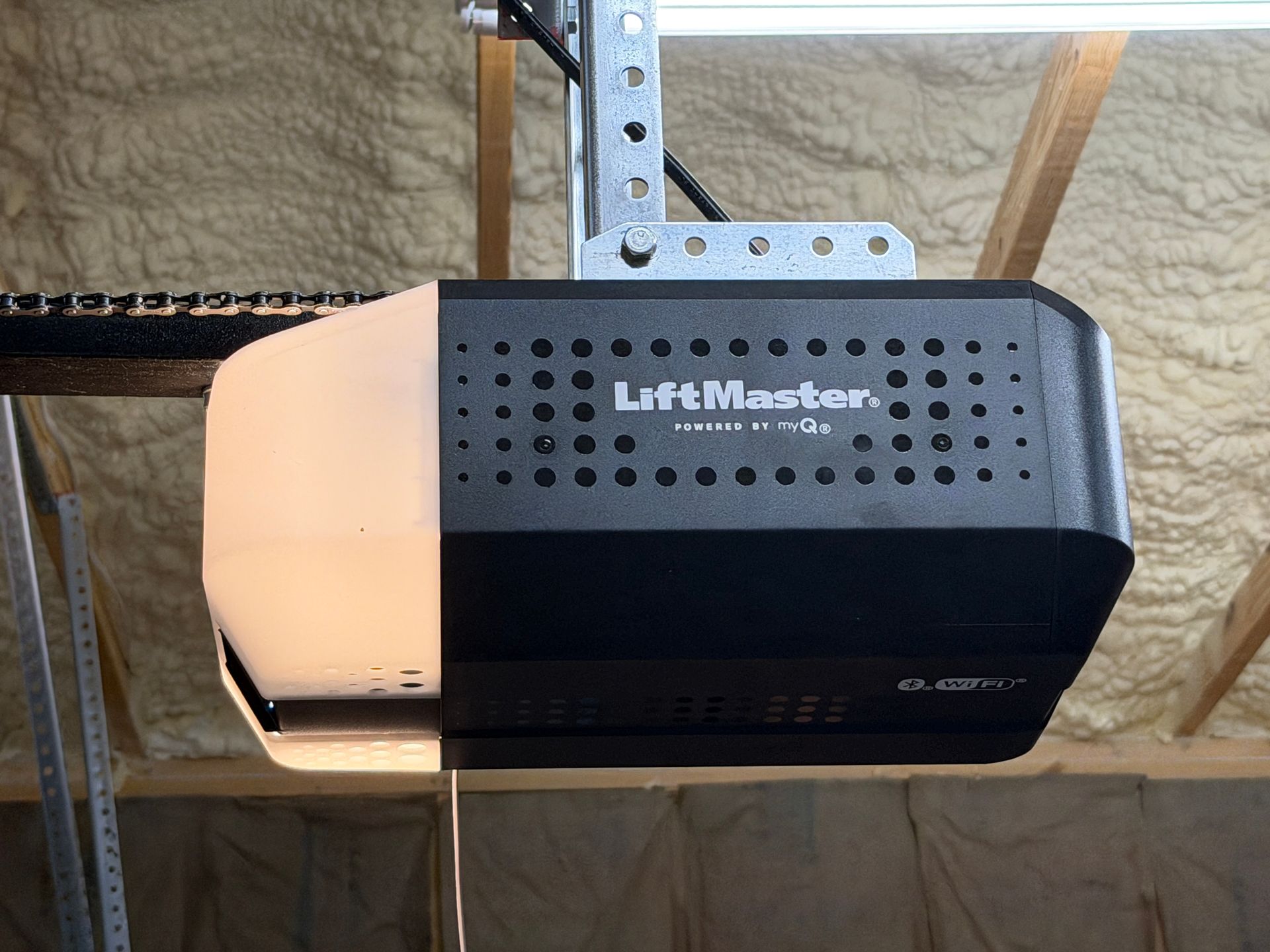 White garage door opener mounted on ceiling with red emergency release cord above a partially open garage door White garage door opener mounted on ceiling with red emergency release cord above a partially open garage door