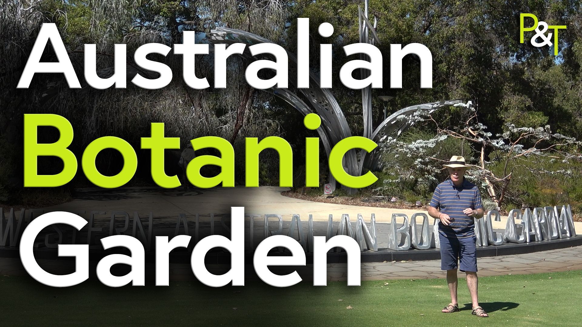 wide shot of the entrance to the Western Australia Botanic garden. There's a sign across the ground and grass in front of it. Behind is the entrance to the gardens with large metal sculptures arching over it. Martin Fish stands to the right of frame in front of the sign, wearing a brimmed hat. The text Australian Botanic Garden in large white and green text over the whole left of the screen. 