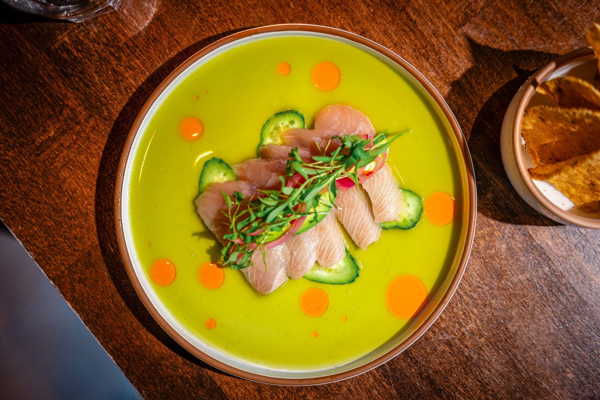 Gourmet fish dish in a green sauce, garnished with herbs on a wooden table, with bread nearby