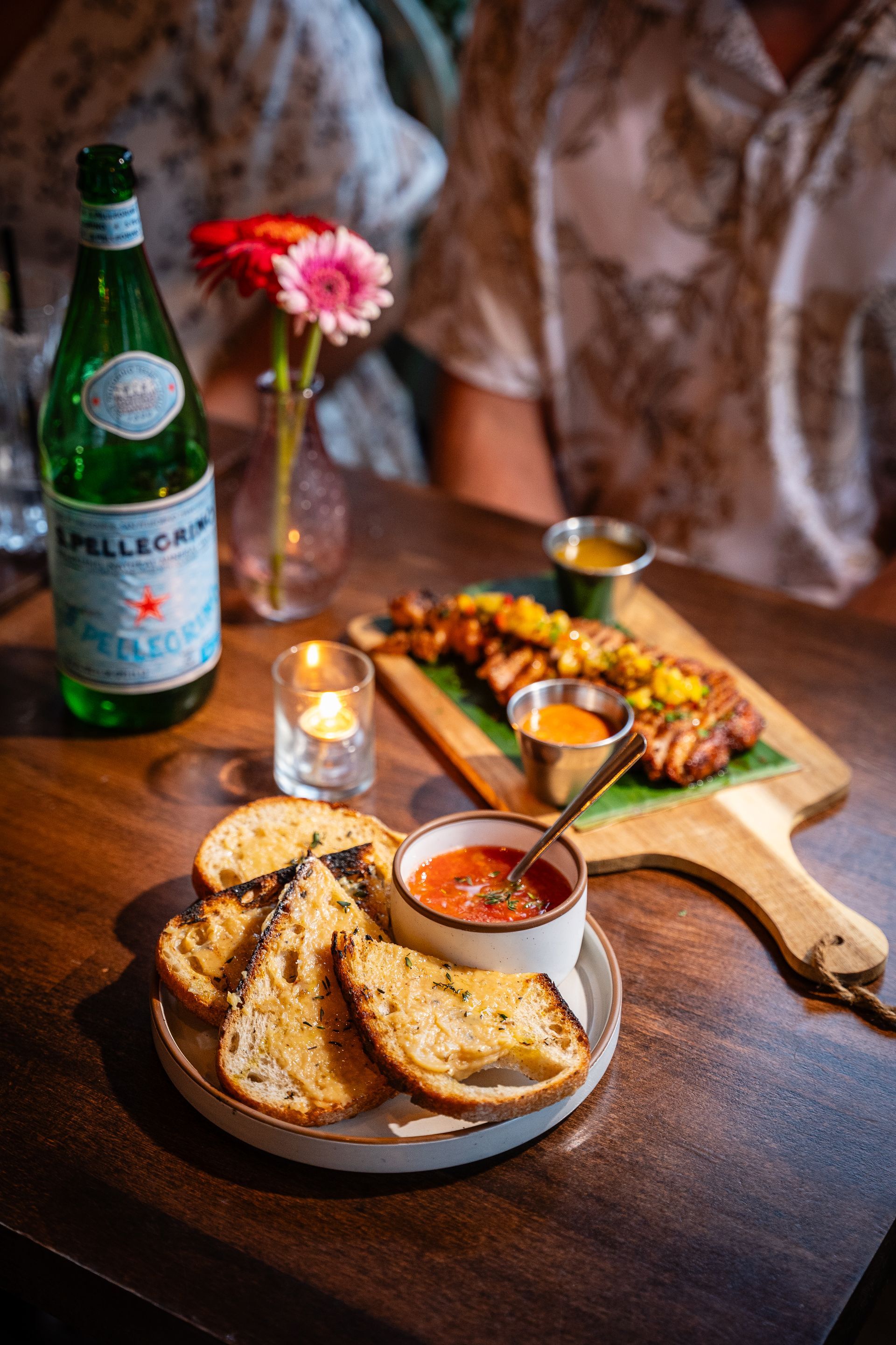 Bread and dip on a dark table with a green bottle, candle, flowers, and a small skillet dish