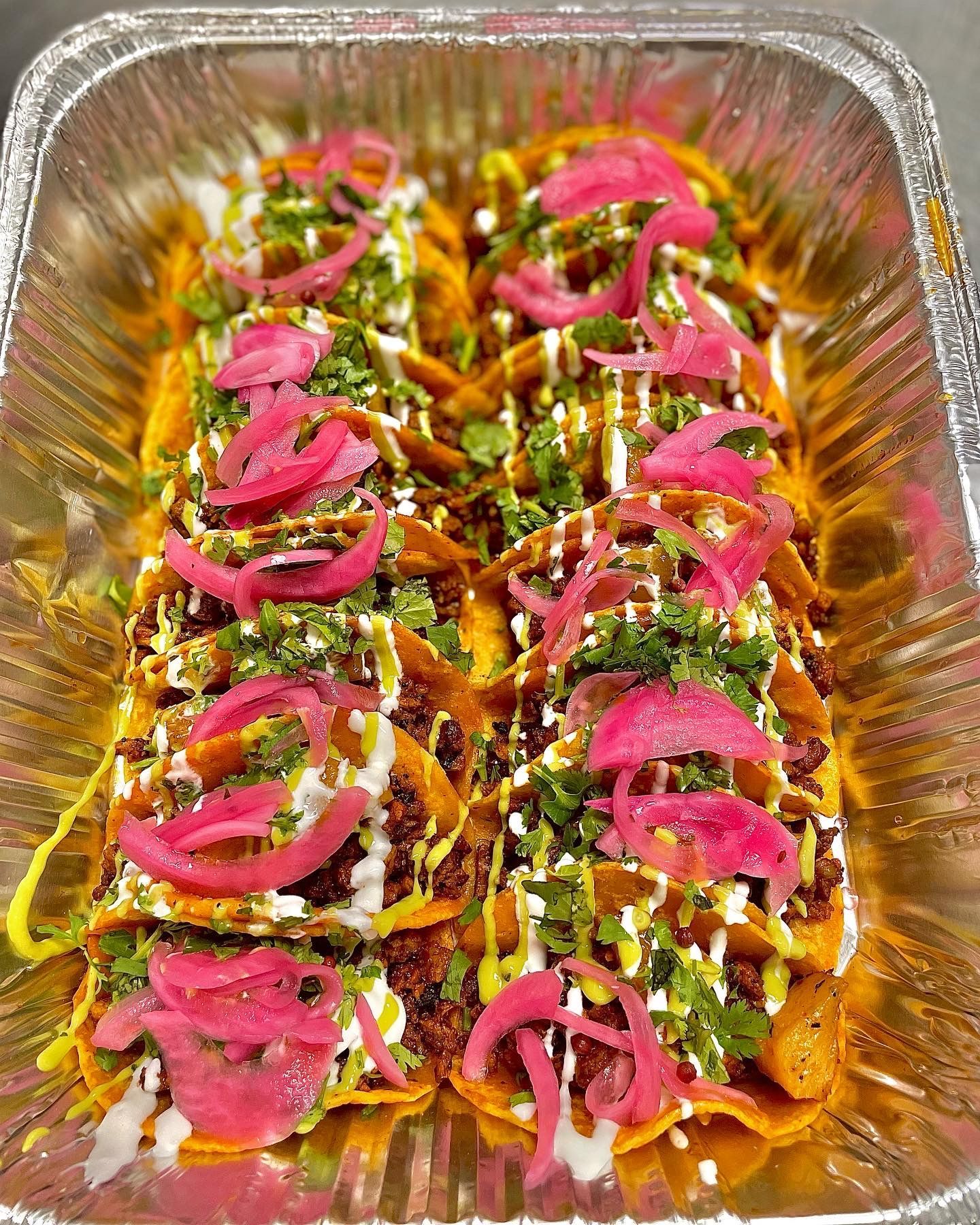 Tray of loaded nachos topped with pink pickled onions, cilantro, cheese, and sauce