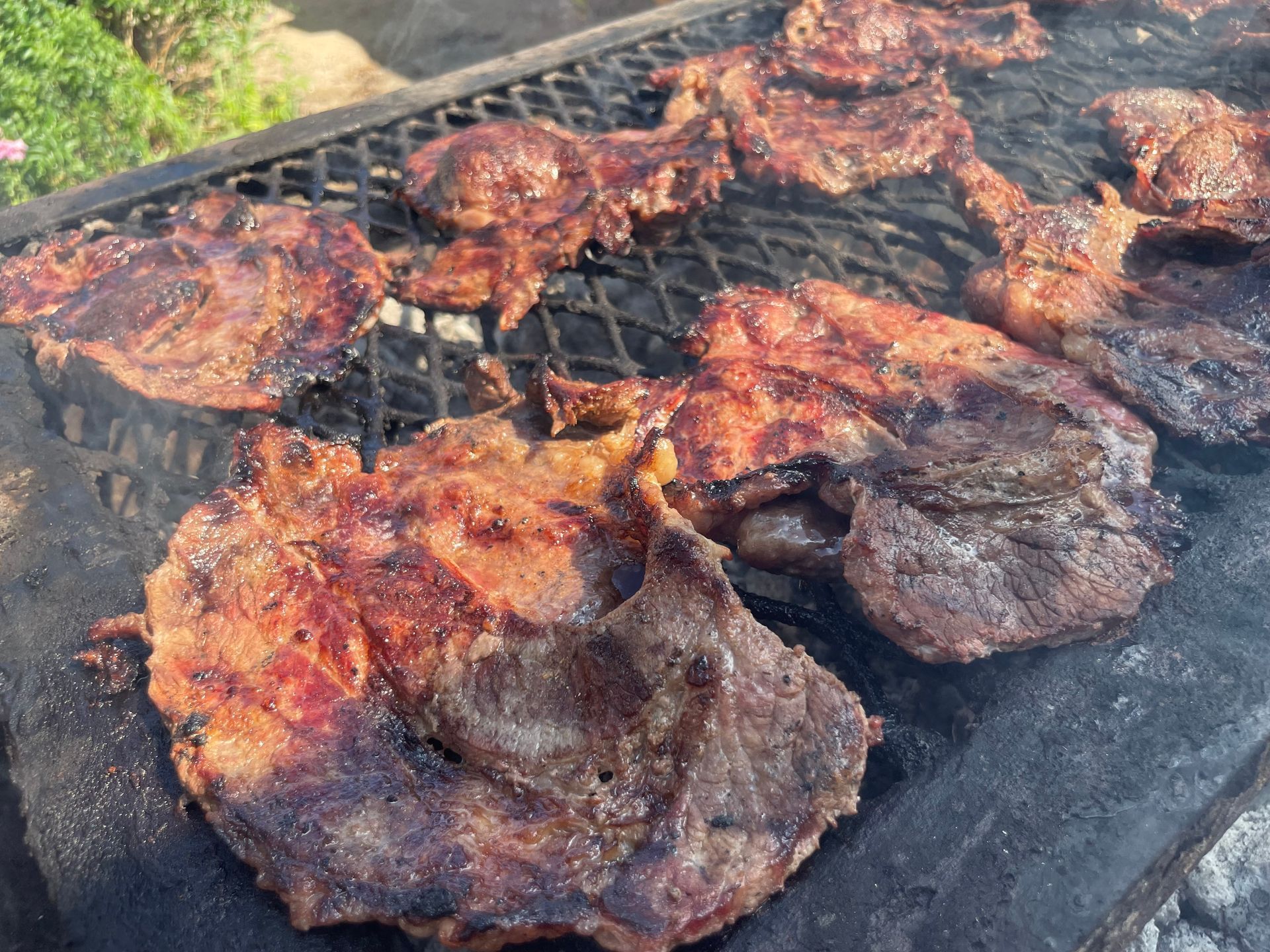 Charred grilled meat patties sizzling on a barbecue grate outdoors