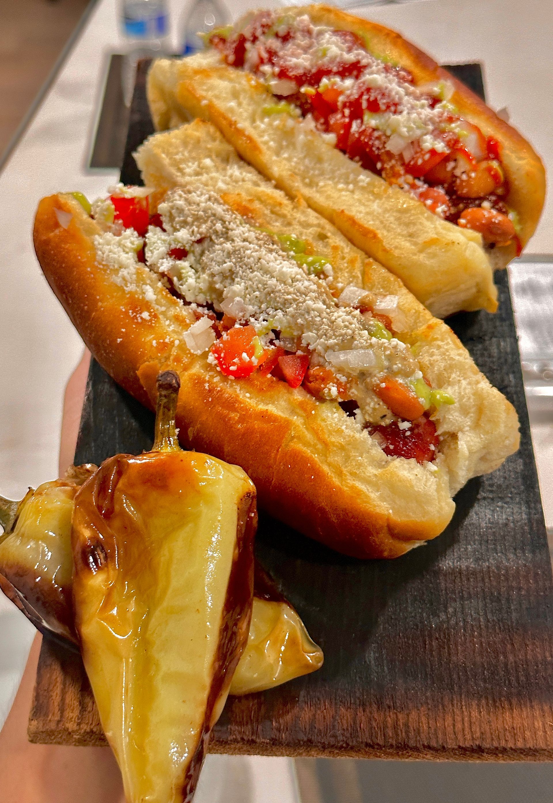 Bacon-wrapped Sonoran hot dogs topped with beans, jalapeños, crema, and salsa. Mexican food catering near me.
