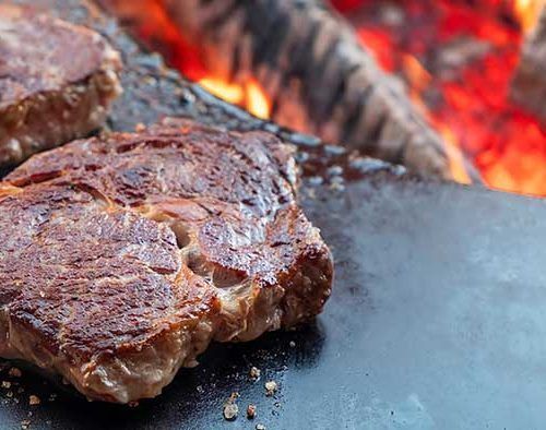 Grilled steak searing over glowing coals on a barbecue grill
