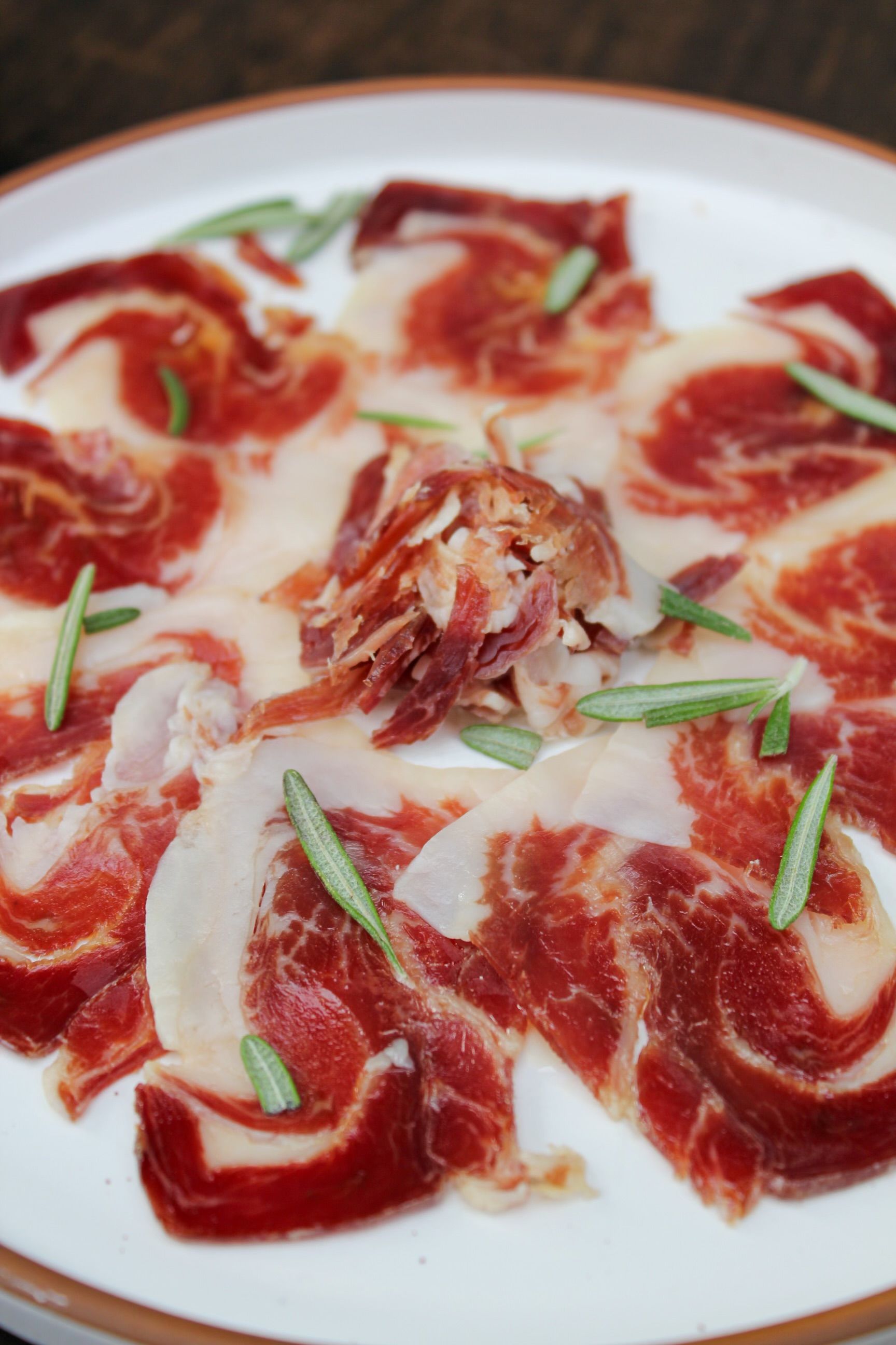 Marinated raw beef slices topped with rosemary in a creamy sauce on a white plate