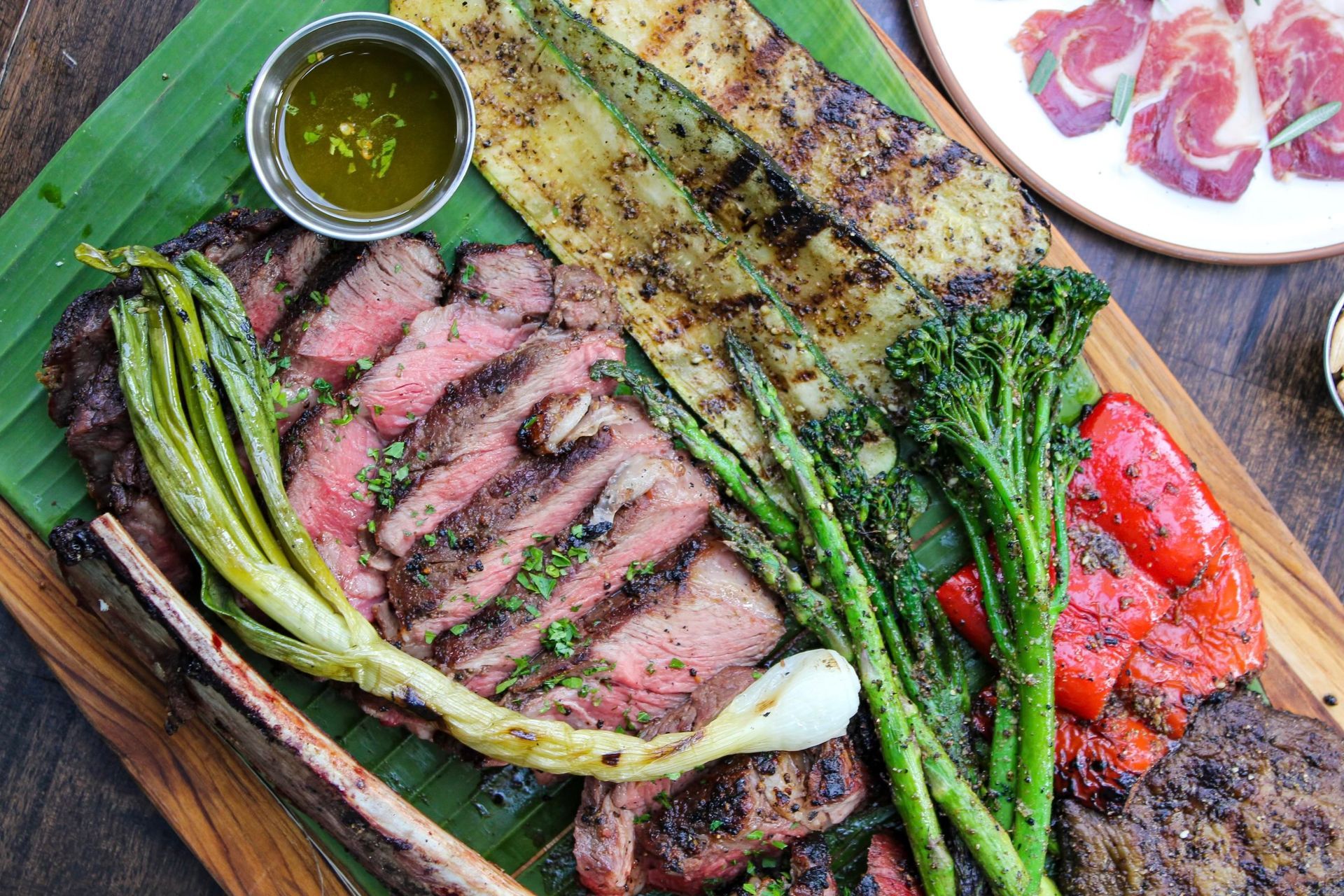 Grilled steak with asparagus, charred peppers, and green sauce on a wooden board