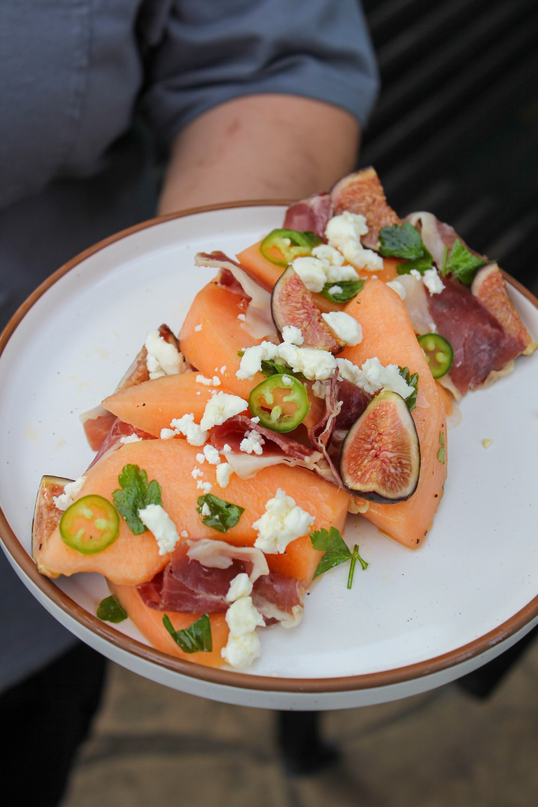 Handheld plate of salmon carpaccio with figs, jalapeños, herbs, and crumbled cheese