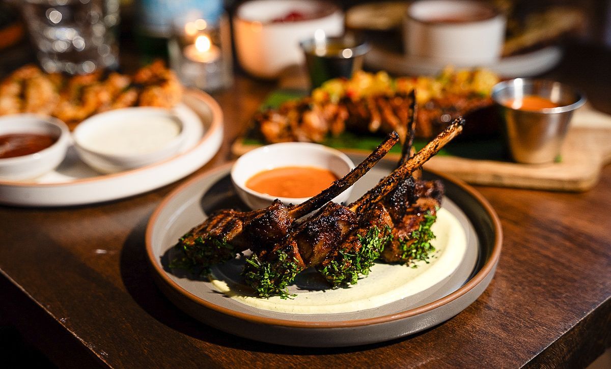 Plated grilled meat with greens and sauce on a restaurant table, with other dishes blurred in the background