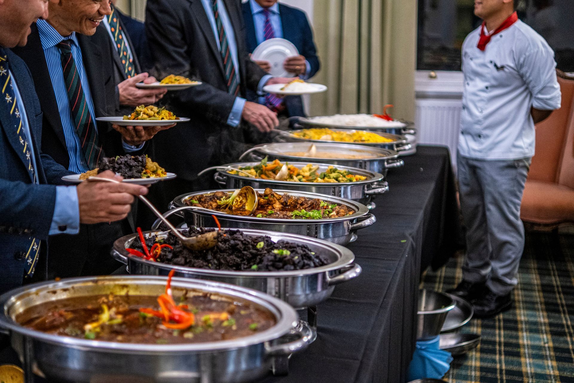 Buffet line with several catered dishes; people serve themselves in a banquet hall.