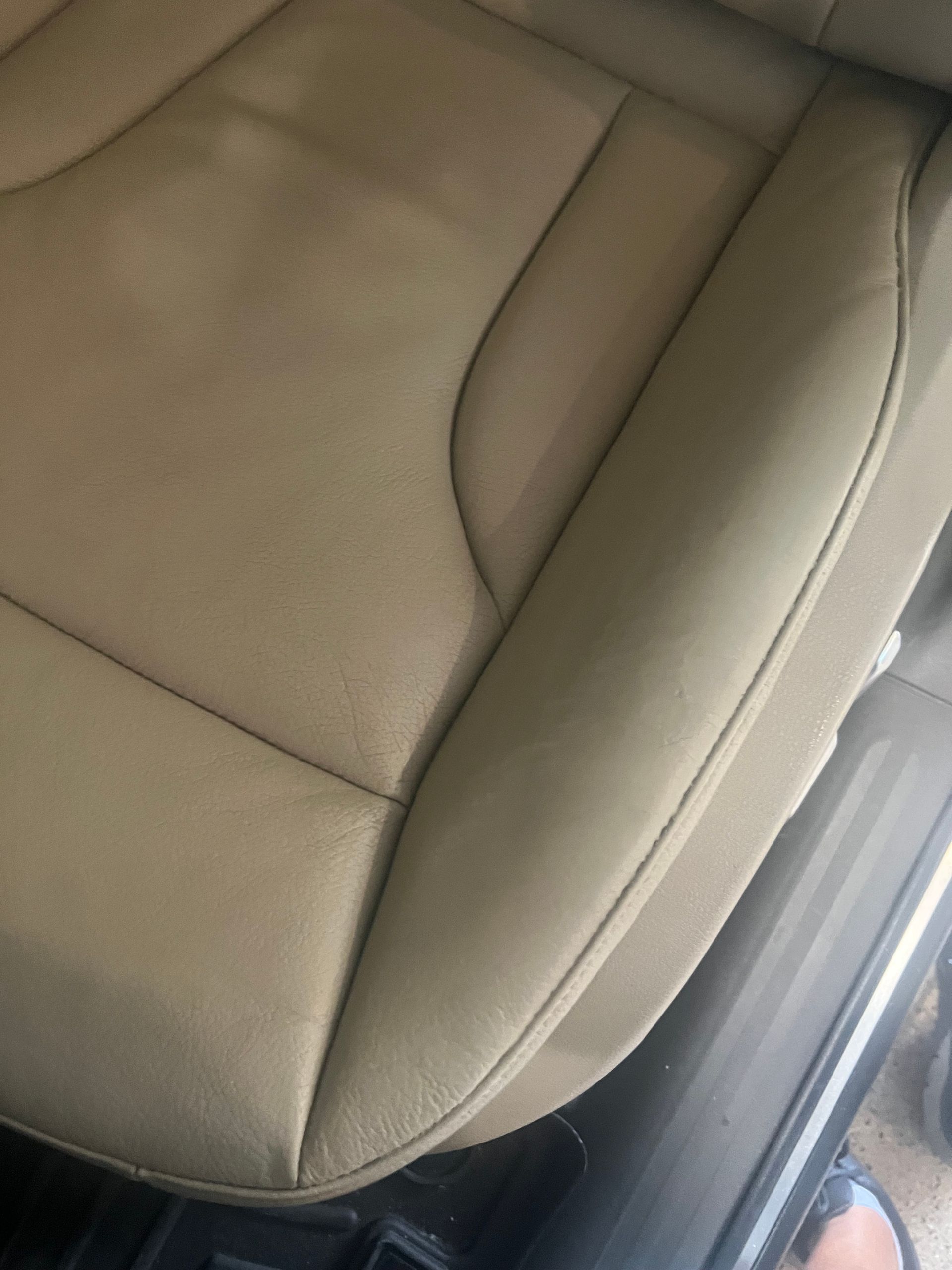 Close-up of a beige car seat with stitched upholstery and a black seat frame.
