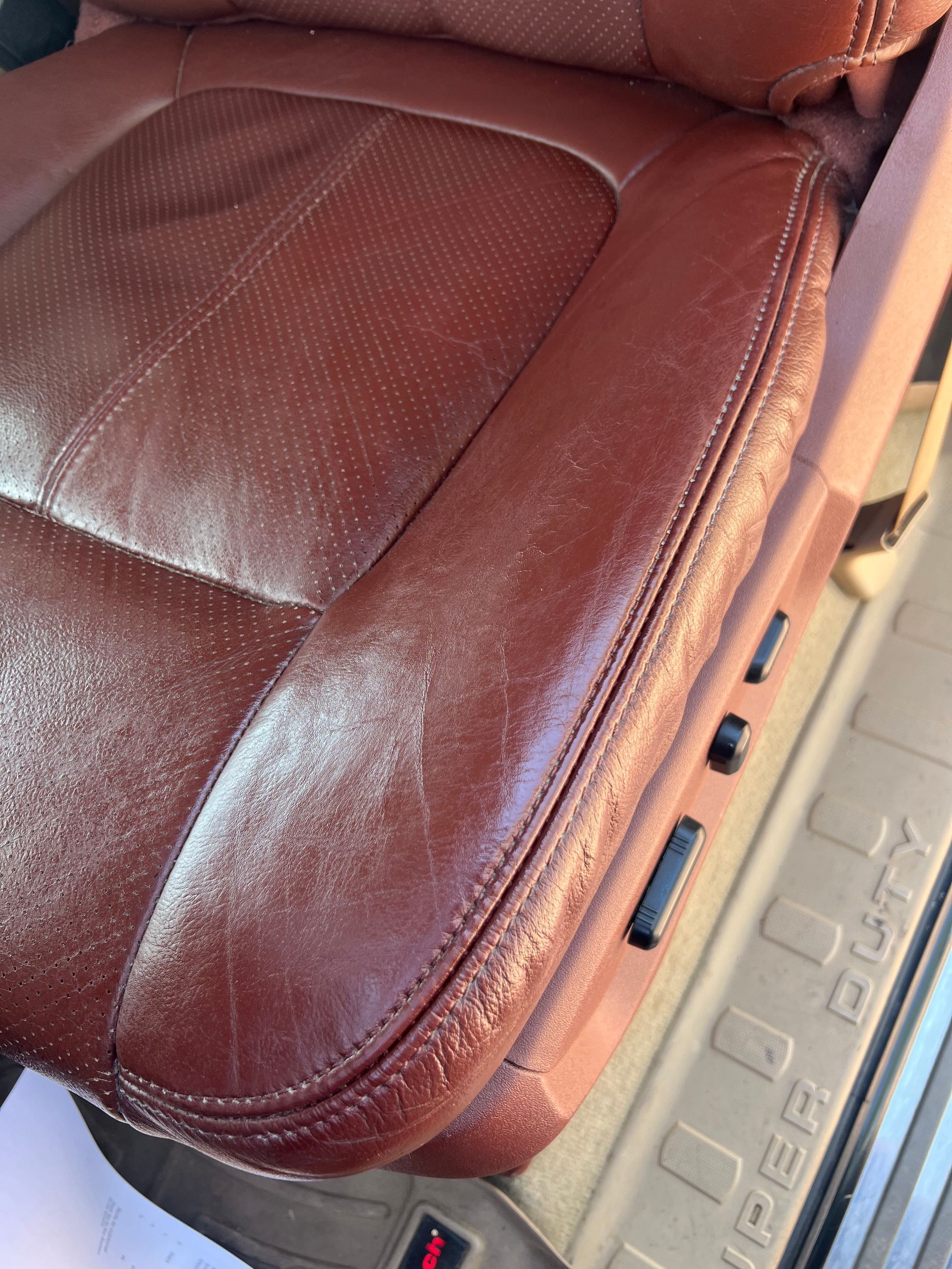 Close-up of a brown leather car seat with visible wear and power seat controls