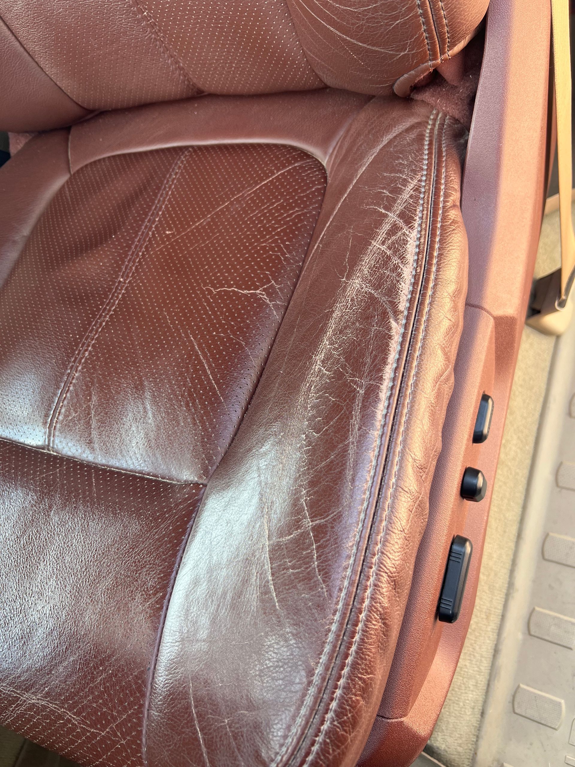 Close-up of a worn brown leather car seat with visible scuffs and stitching