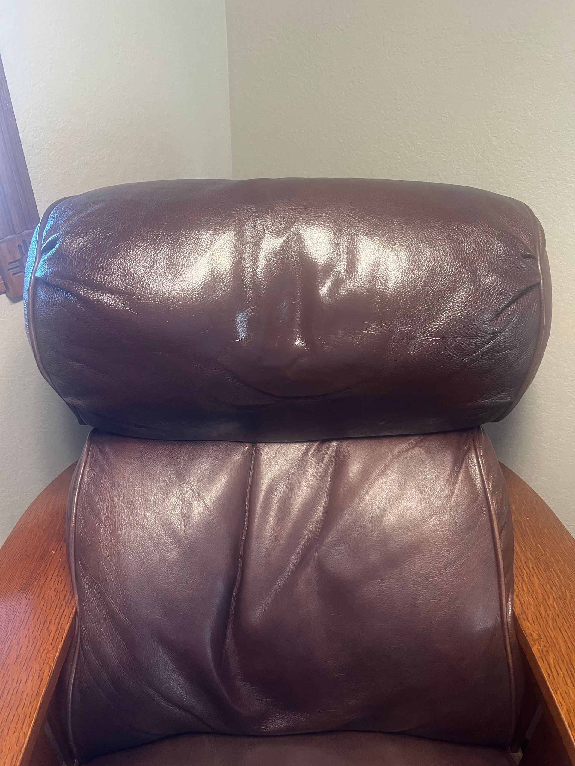 Close-up of a dark brown leather office chair backrest against a beige wall.