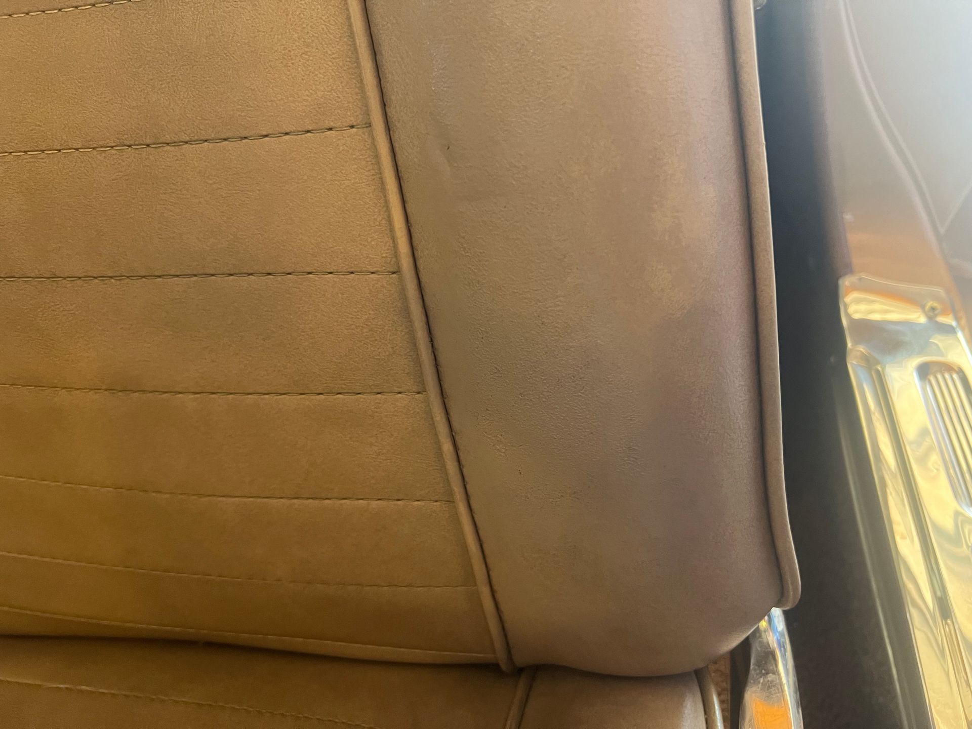 Brown leather car seat with stitched upholstery beside a sunlit window