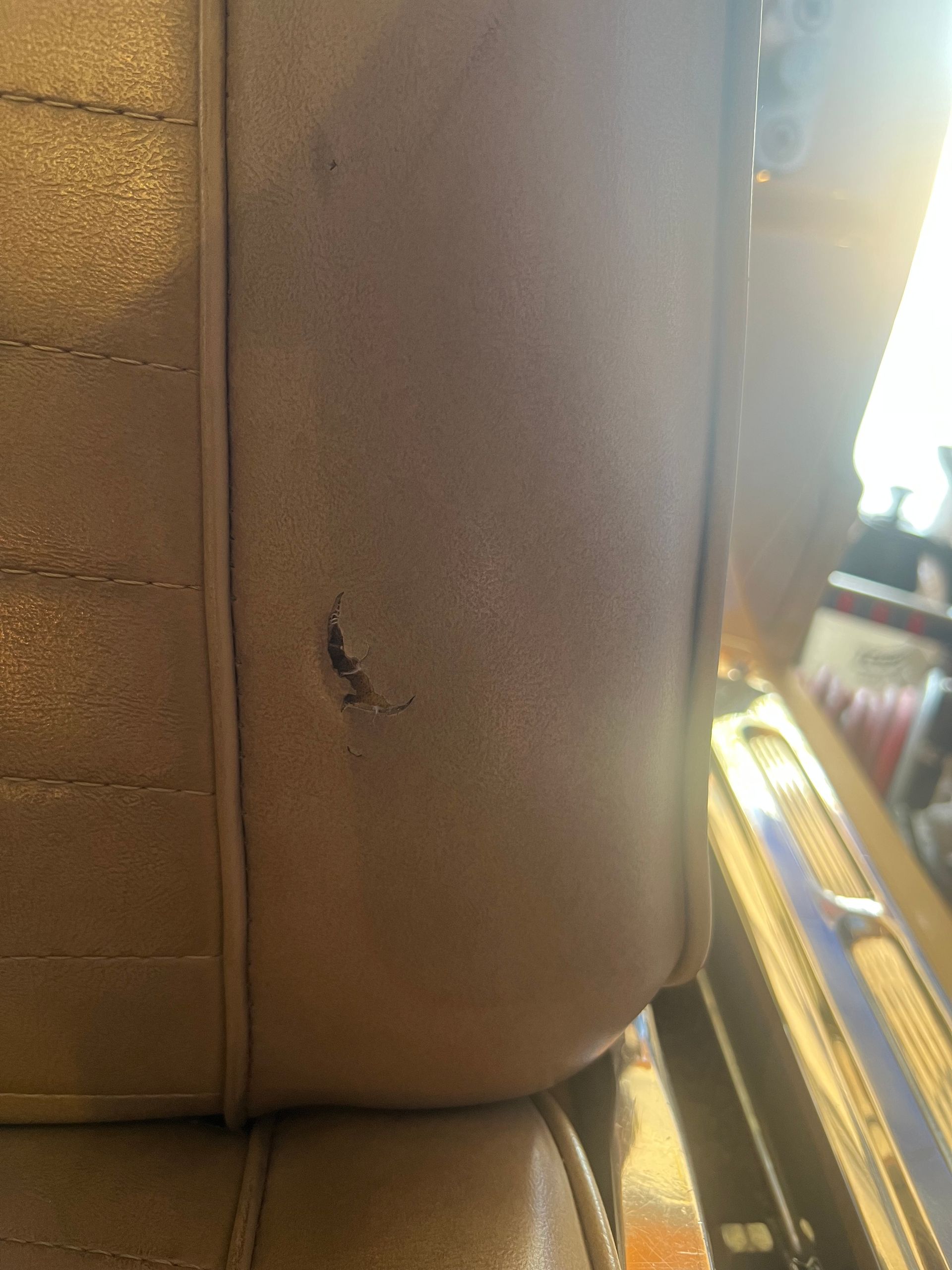 Close-up of a tan leather car seat with a small tear near the seam.