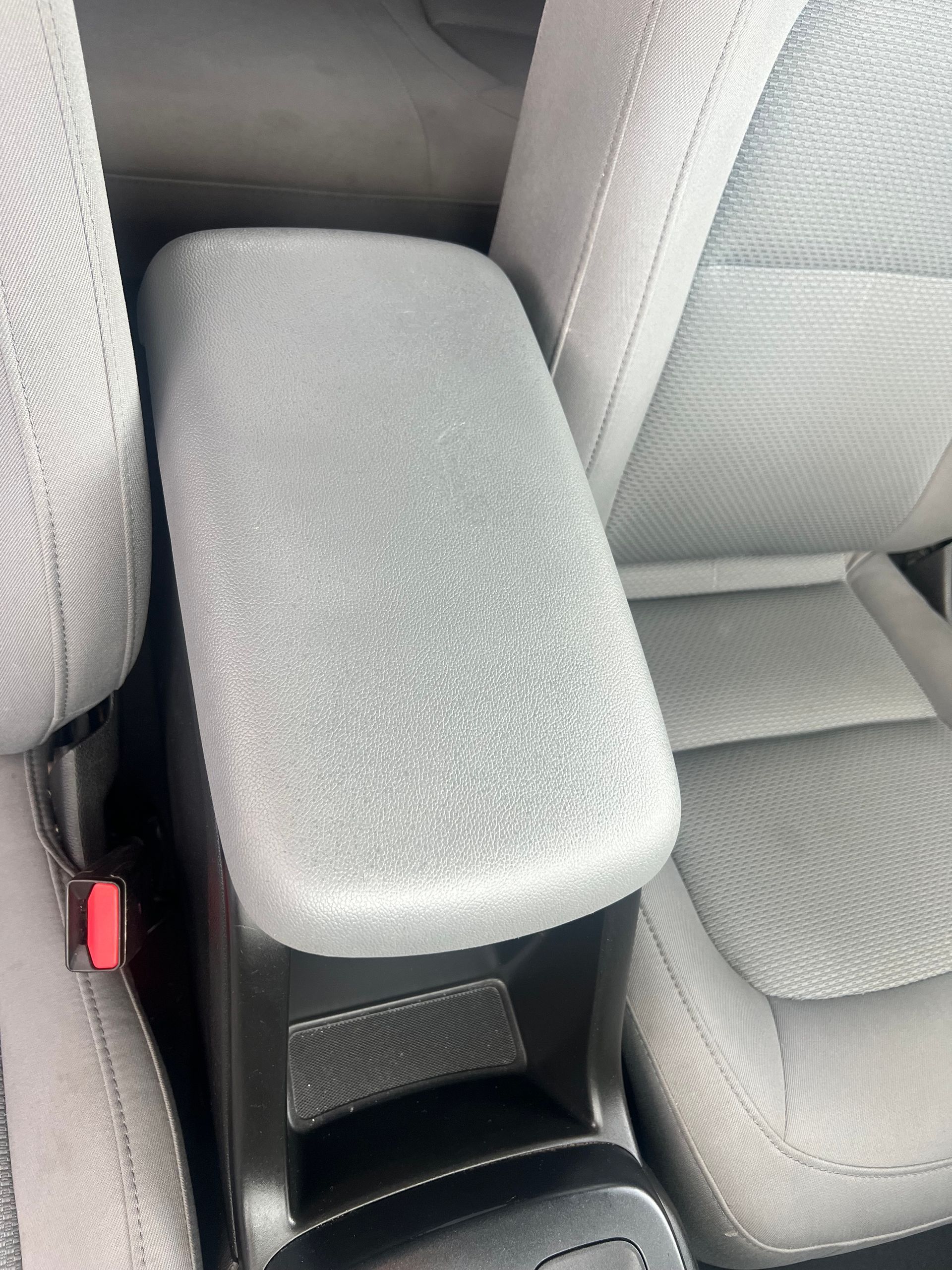 Center console armrest with gray textured cover between car seats.