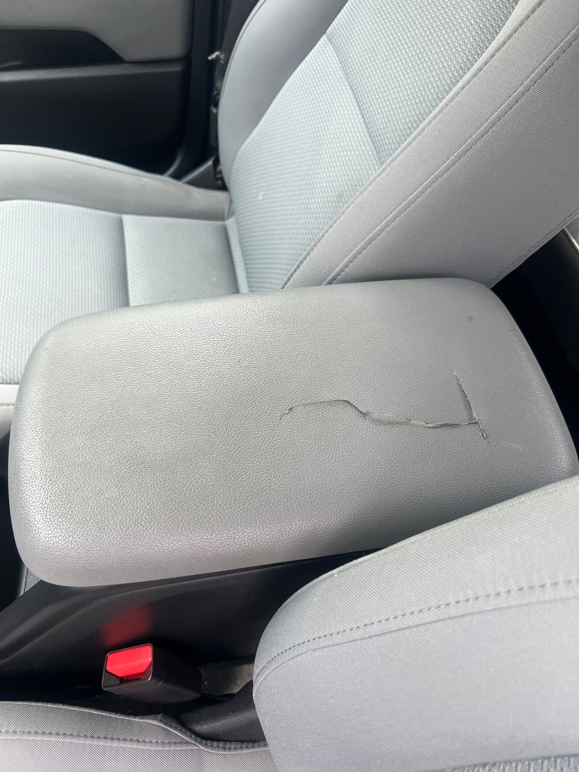 Gray car armrest with a large crack and worn upholstery next to a gray fabric seat.