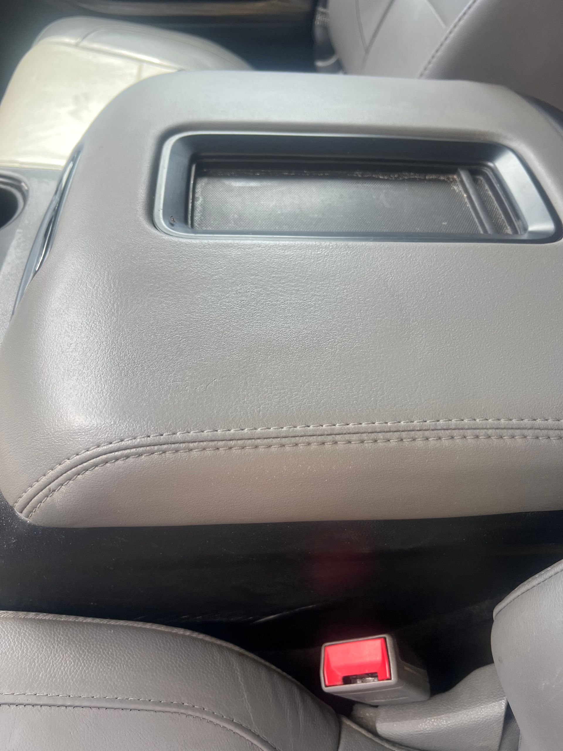 Black car center armrest with built-in handle and red seatbelt buckle visible below