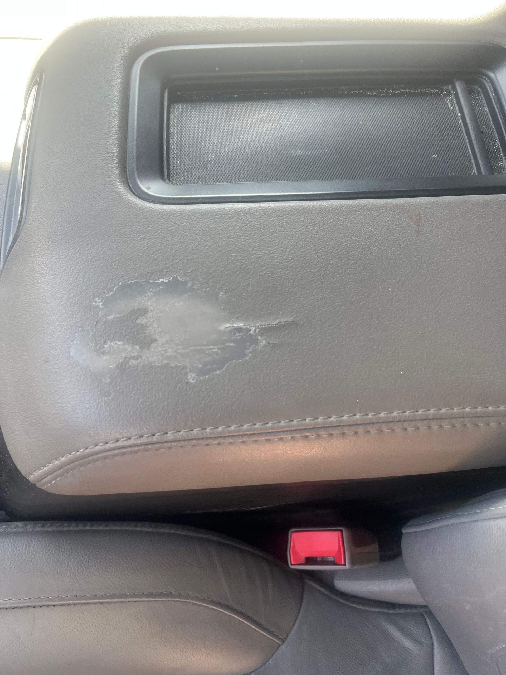 Close-up of a gray car seat with a worn, scuffed patch and red seatbelt buckle below