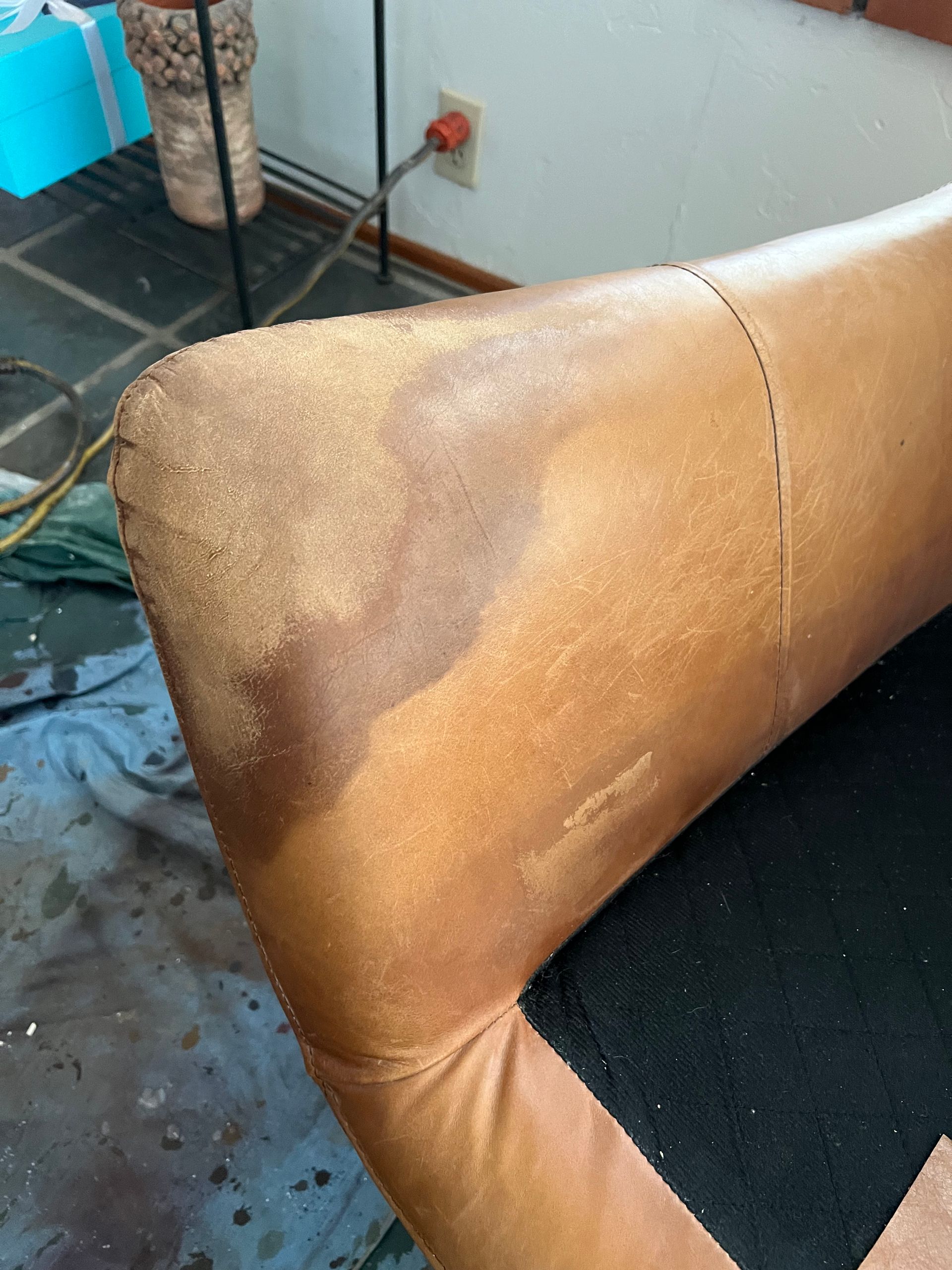 Brown leather sofa armrest with visible wear and a dark seat cushion in a room corner