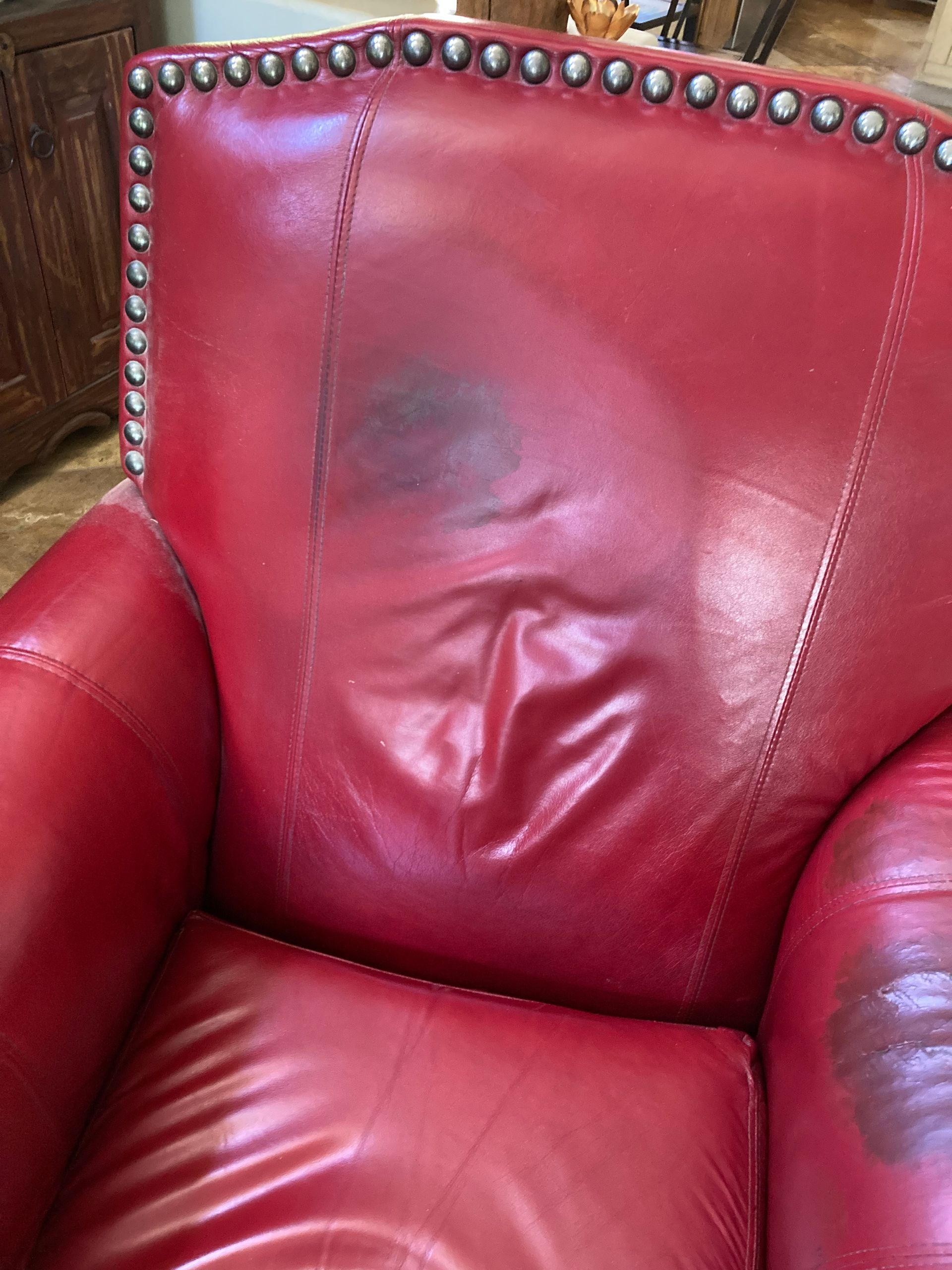 Red leather armchair with dark stains on the back and seat, shown close up.