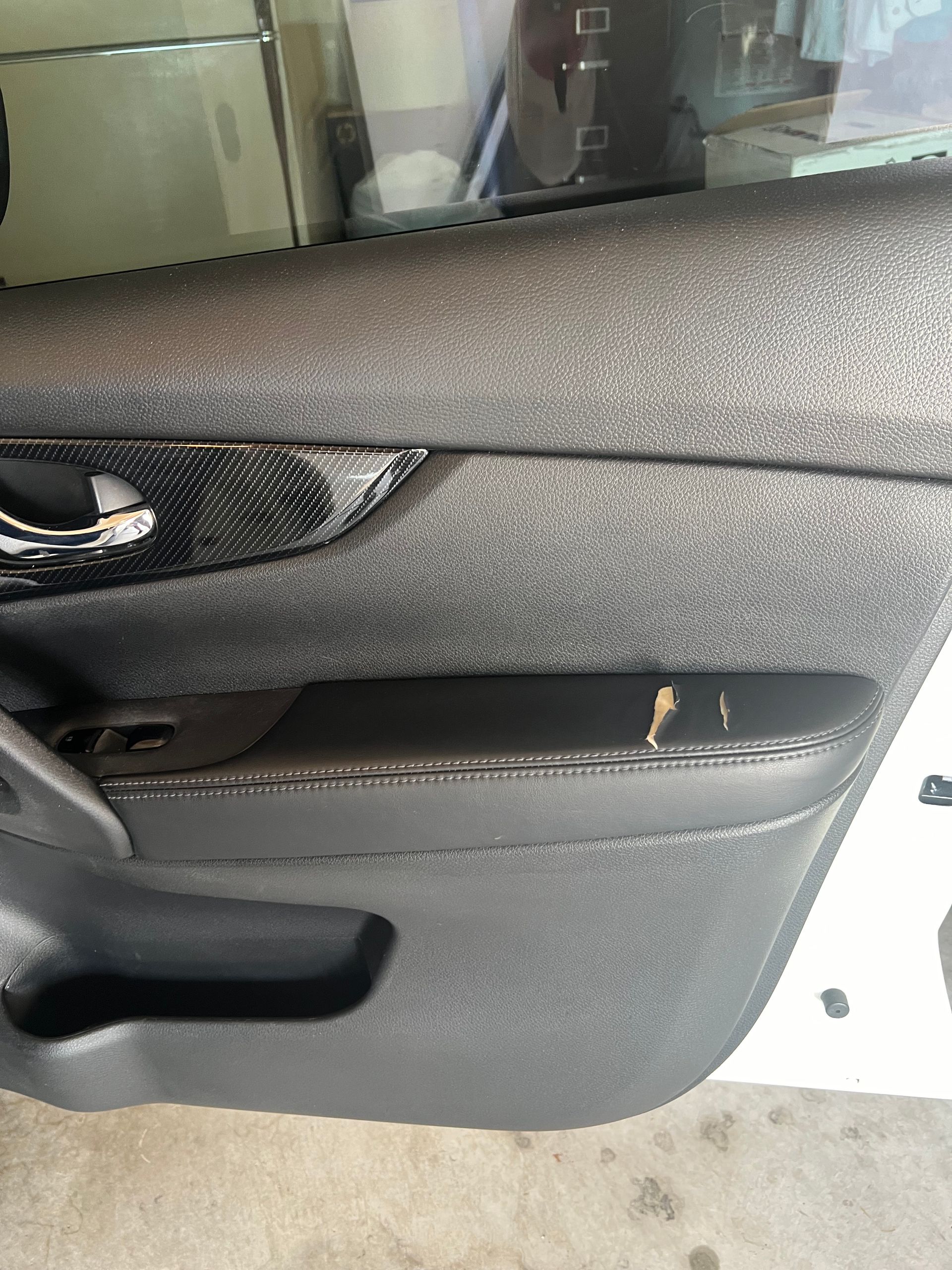 Close-up of a black car door interior with a damaged armrest trim piece peeled back.