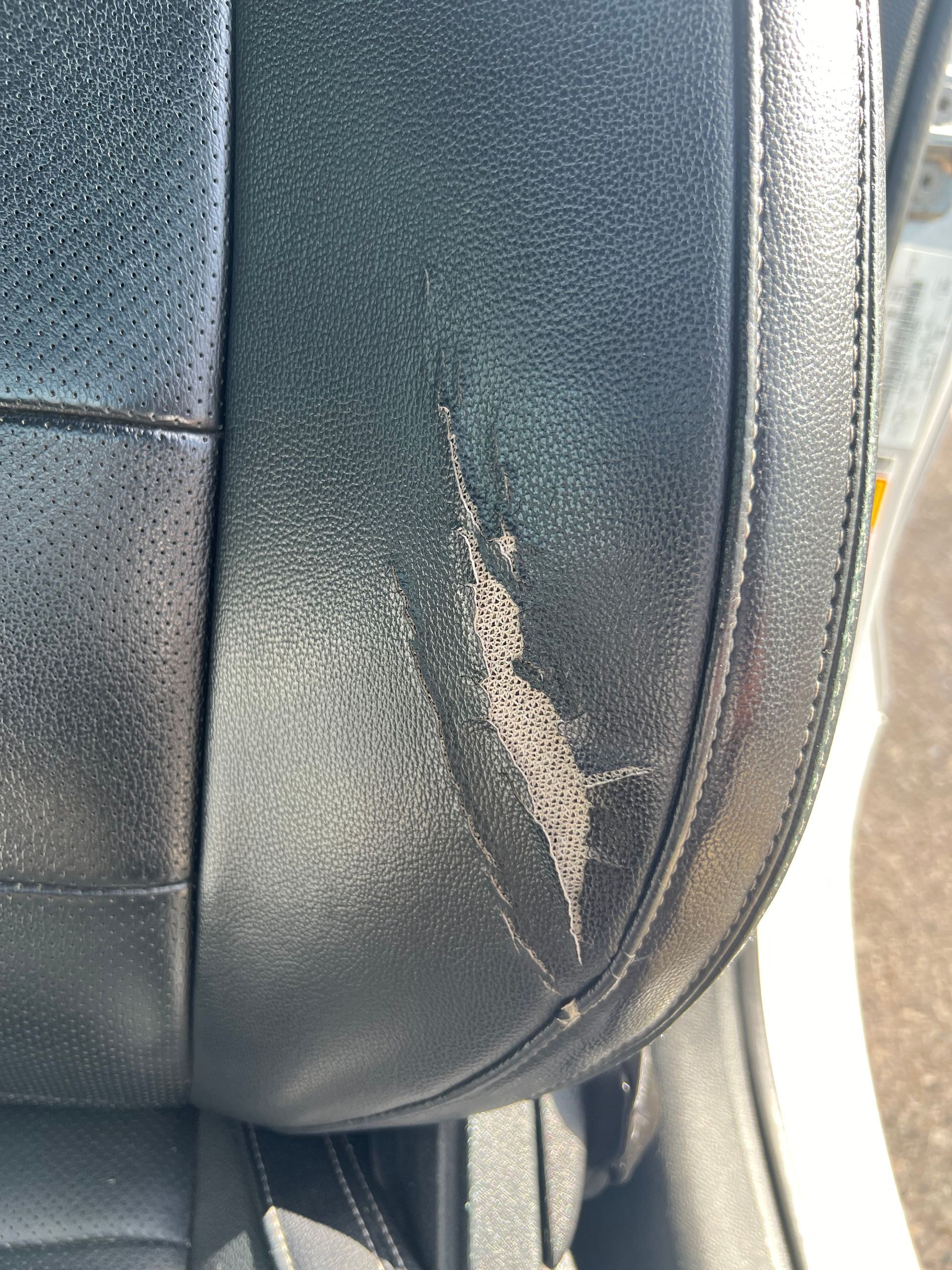 Close-up of a worn black leather seat with a torn and scuffed side seam