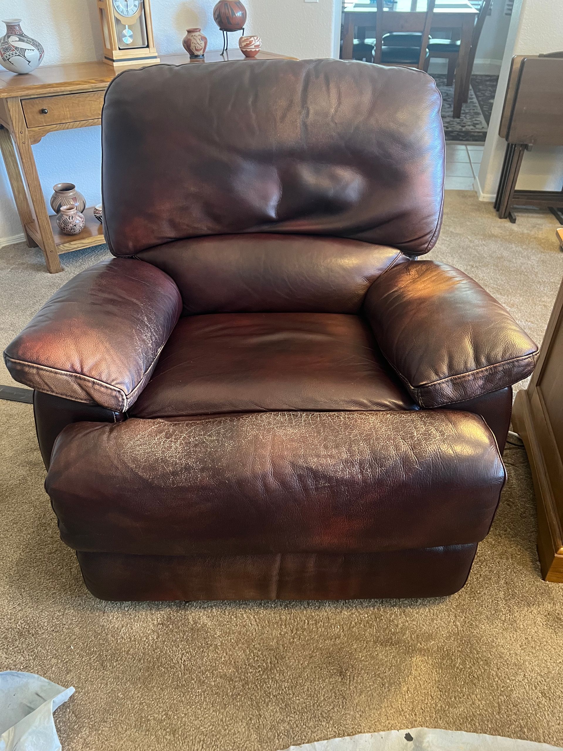 Brown leather recliner chair in a living room with carpet and furniture in the background