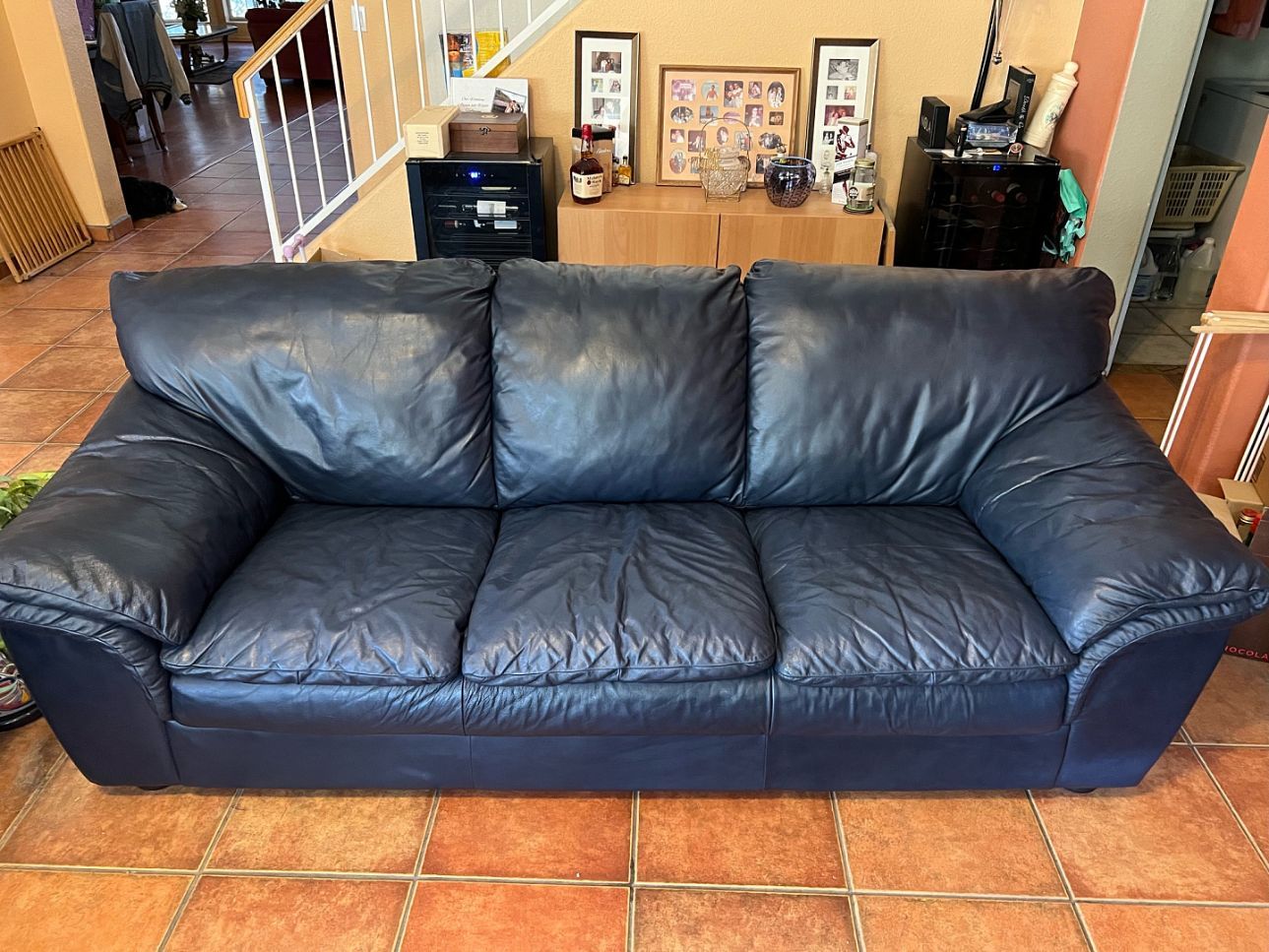 Blue leather couch in a living room with tiled floor and framed art in the background