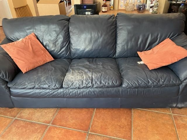 Black leather sofa with two orange throw pillows on a tiled floor.