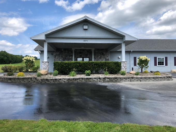 Front entrance of a gray building with a covered driveway and wet pavement after rain