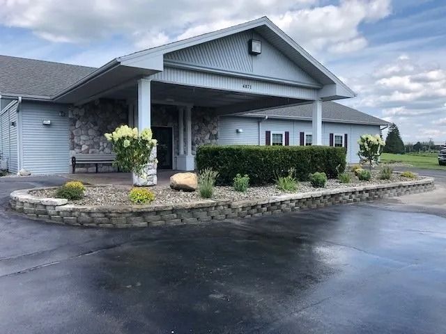 Gray building with covered entrance and landscaped stone planter beside a wet driveway