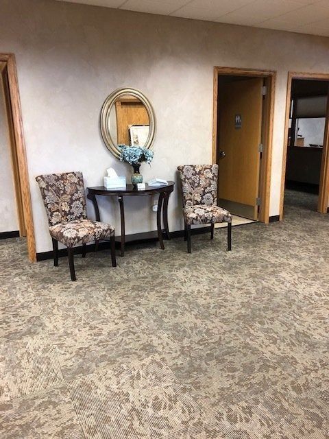 Small lobby with two patterned chairs, a round mirror, and open doorways on a carpeted floor.