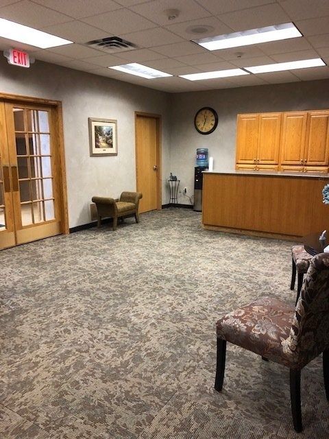 Small office lobby with reception desk, patterned carpet, chairs, and wall clock.