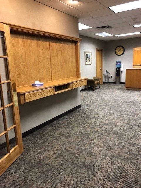 Empty office lobby with a wooden mail counter, carpeted floor, and wall clock near the hallway