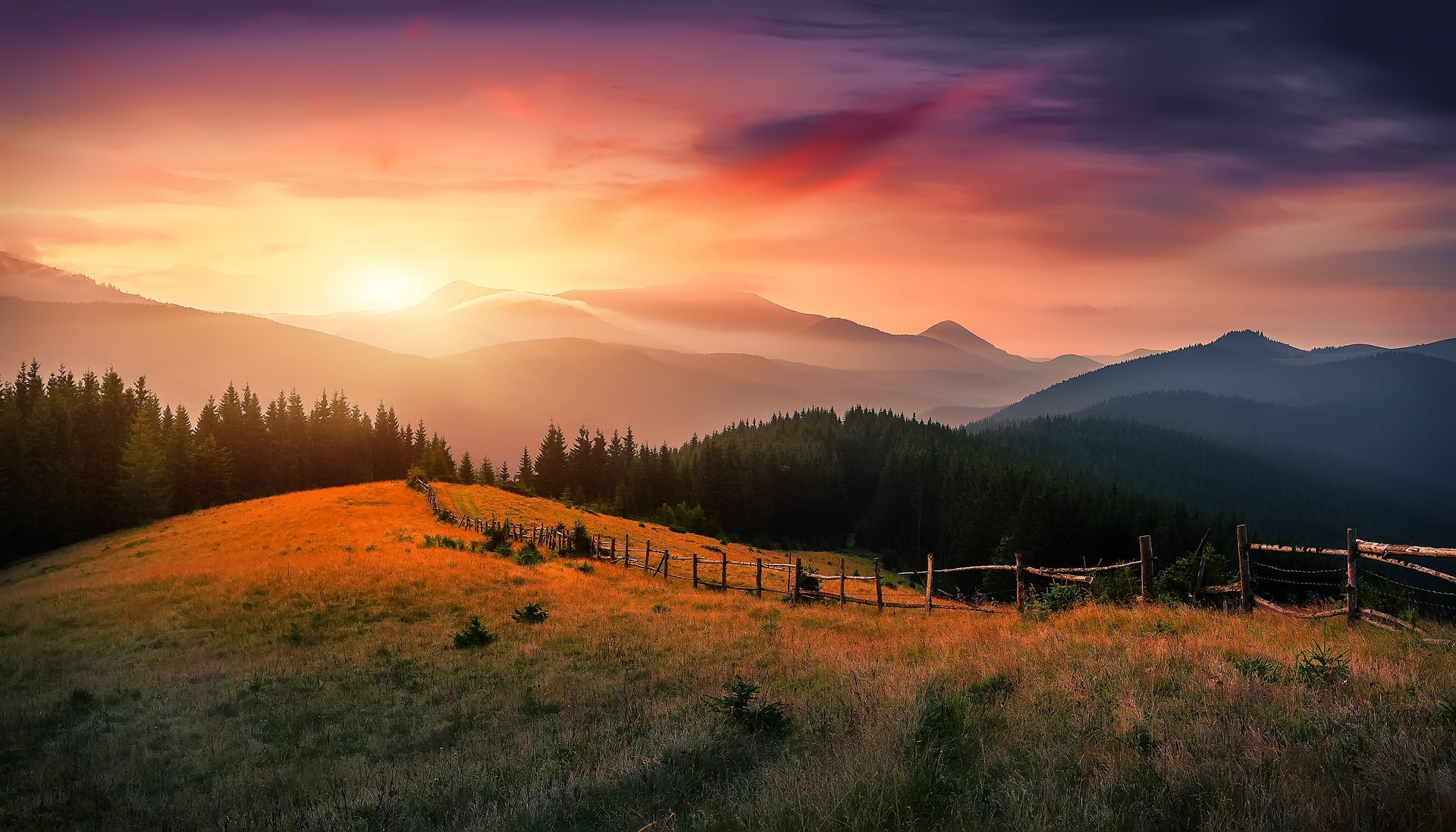 Sunset over rolling hills with a glowing orange meadow and distant mountains