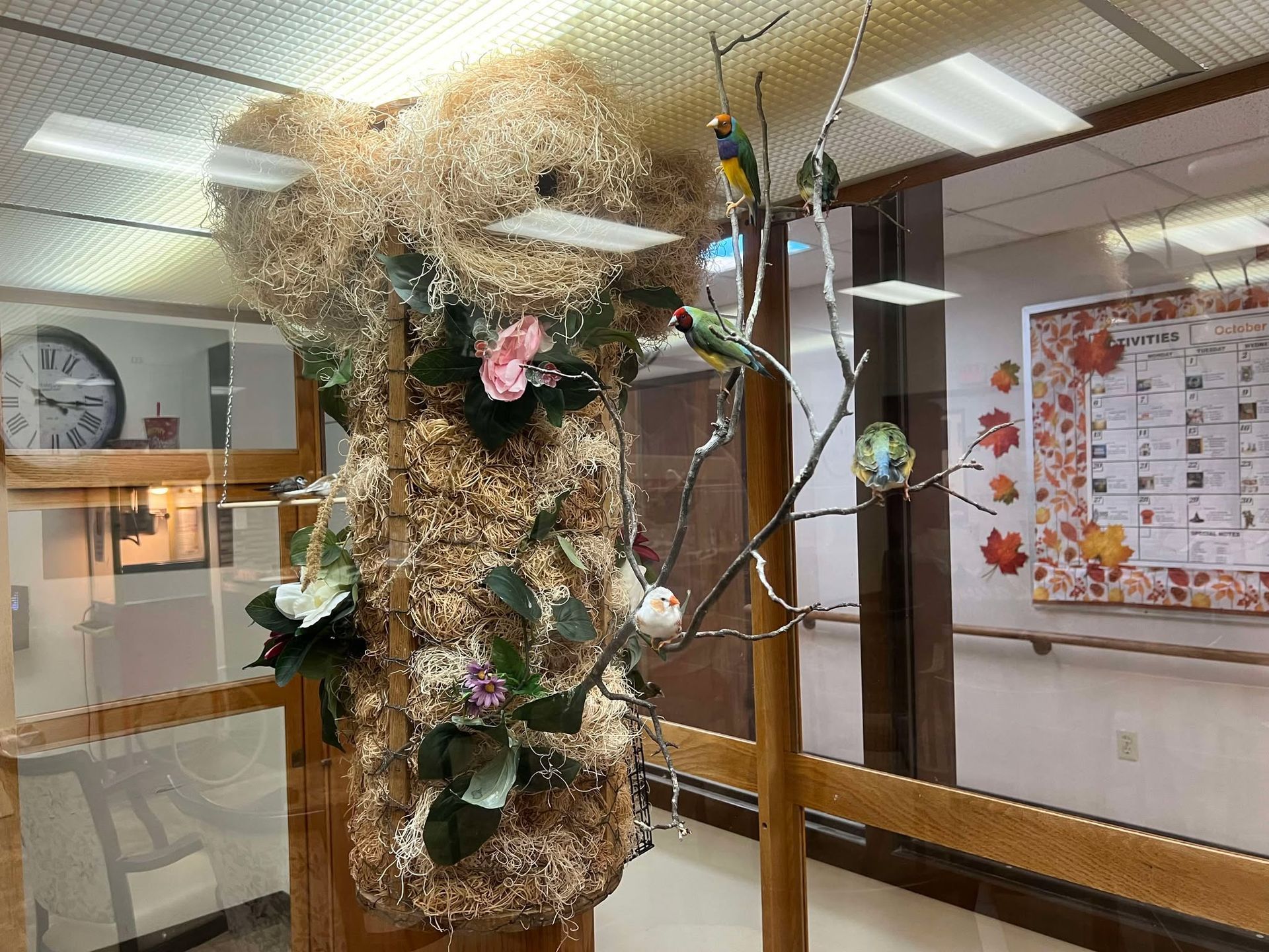 A room with a clock on the wall and a tree made of flowers and leaves.