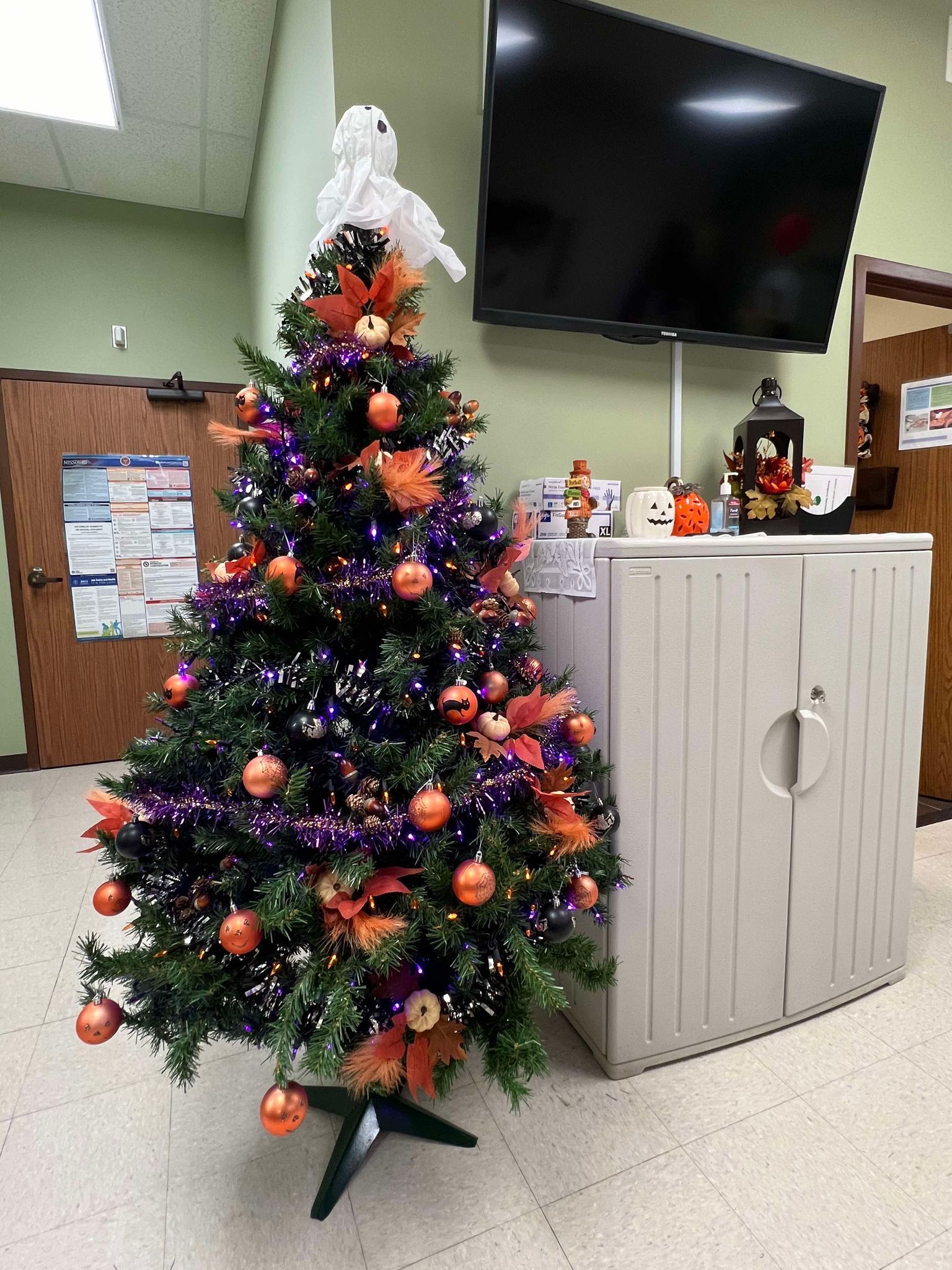 A christmas tree decorated for halloween is sitting in a room next to a tv.