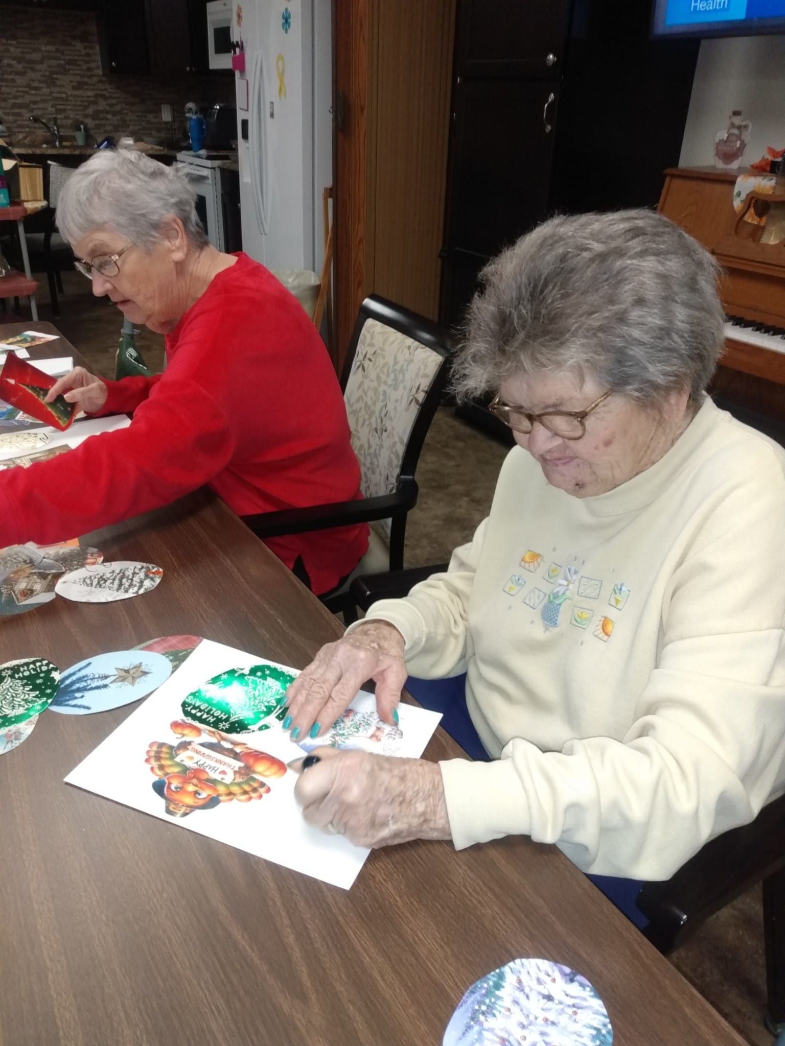 Two older women are sitting at a table painting.