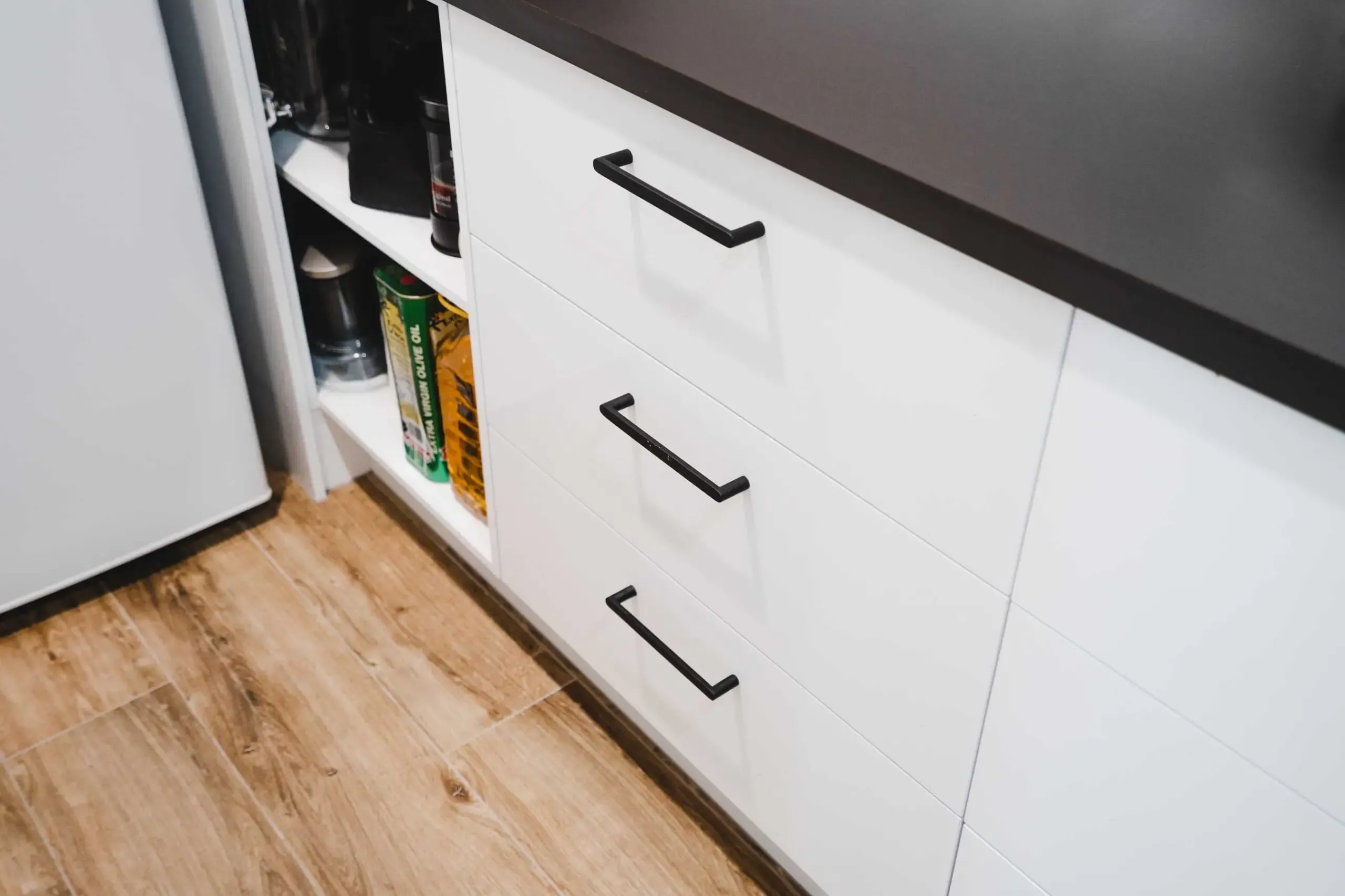 A Kitchen With White Cabinets and Black Handles and a Wooden Floor — CK Cabinetry in Coolum Beach, QLD