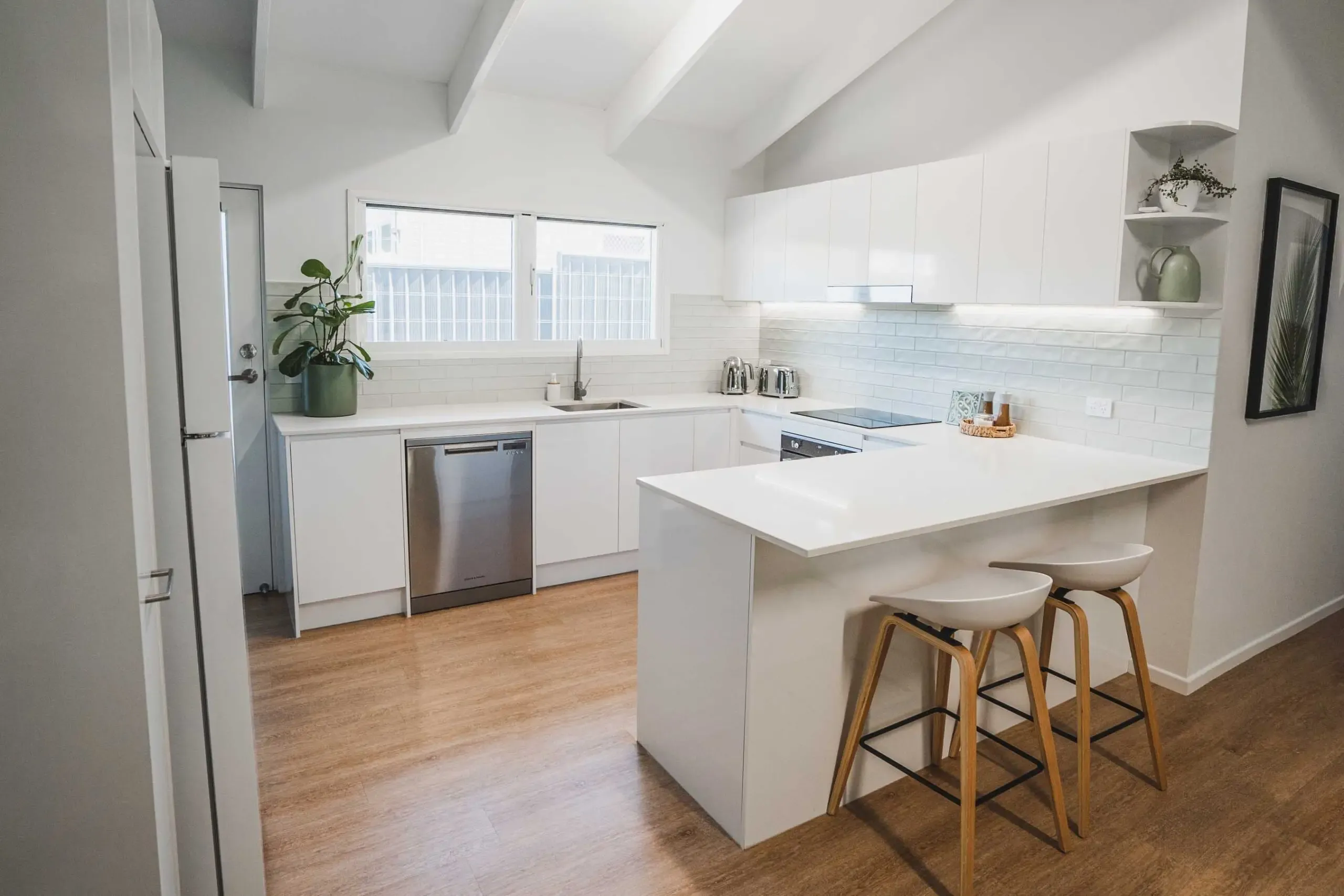 A Kitchen With White Cabinets and Wooden Floors and Stools — CK Cabinetry in Coolum Beach, QLD