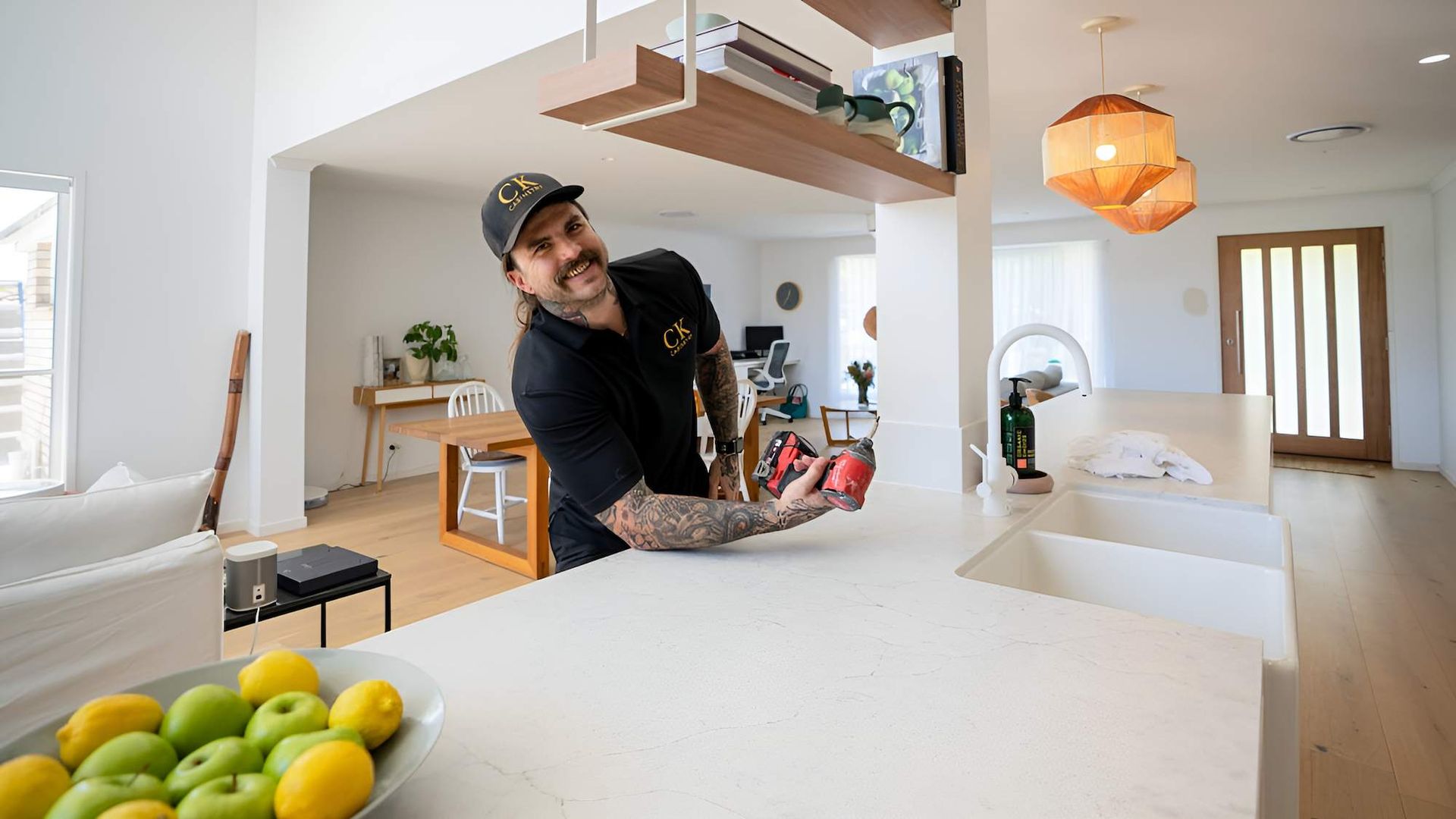 A Man is Standing at a Kitchen Counter Holding a Bottle of Wine — CK Cabinetry in Coolum Beach, QLD