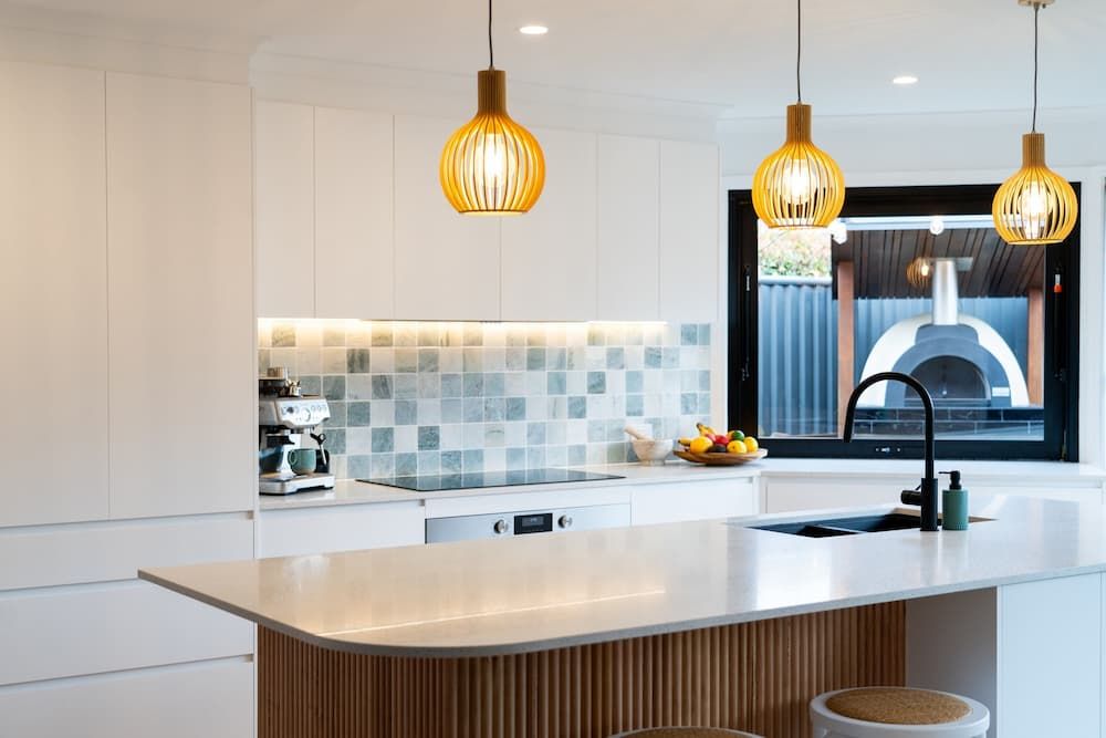 Modern Kitchen With White Cabinetry and a Sleek Island Featuring a Curved Wooden Accent