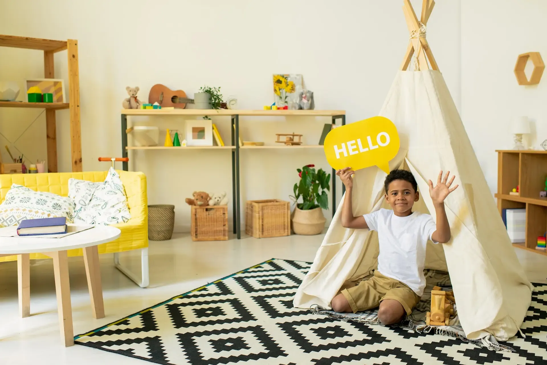 A Young Boy is Sitting in a Teepee in a Living Room Holding a Hello Sign — CK Cabinetry in Coolum Beach, QLD